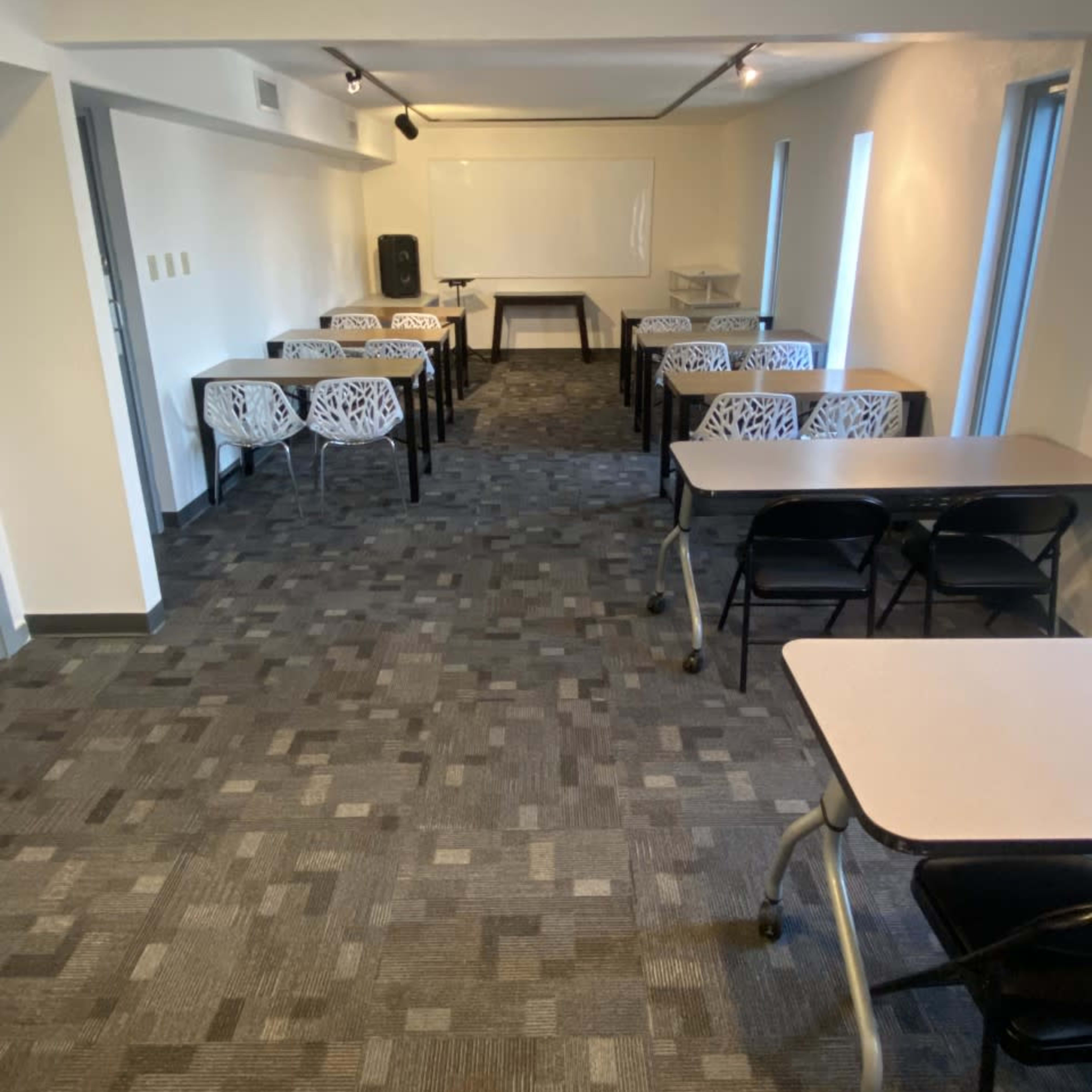 A classroom or meeting room with several tables arranged neatly in rows on a carpeted floor.