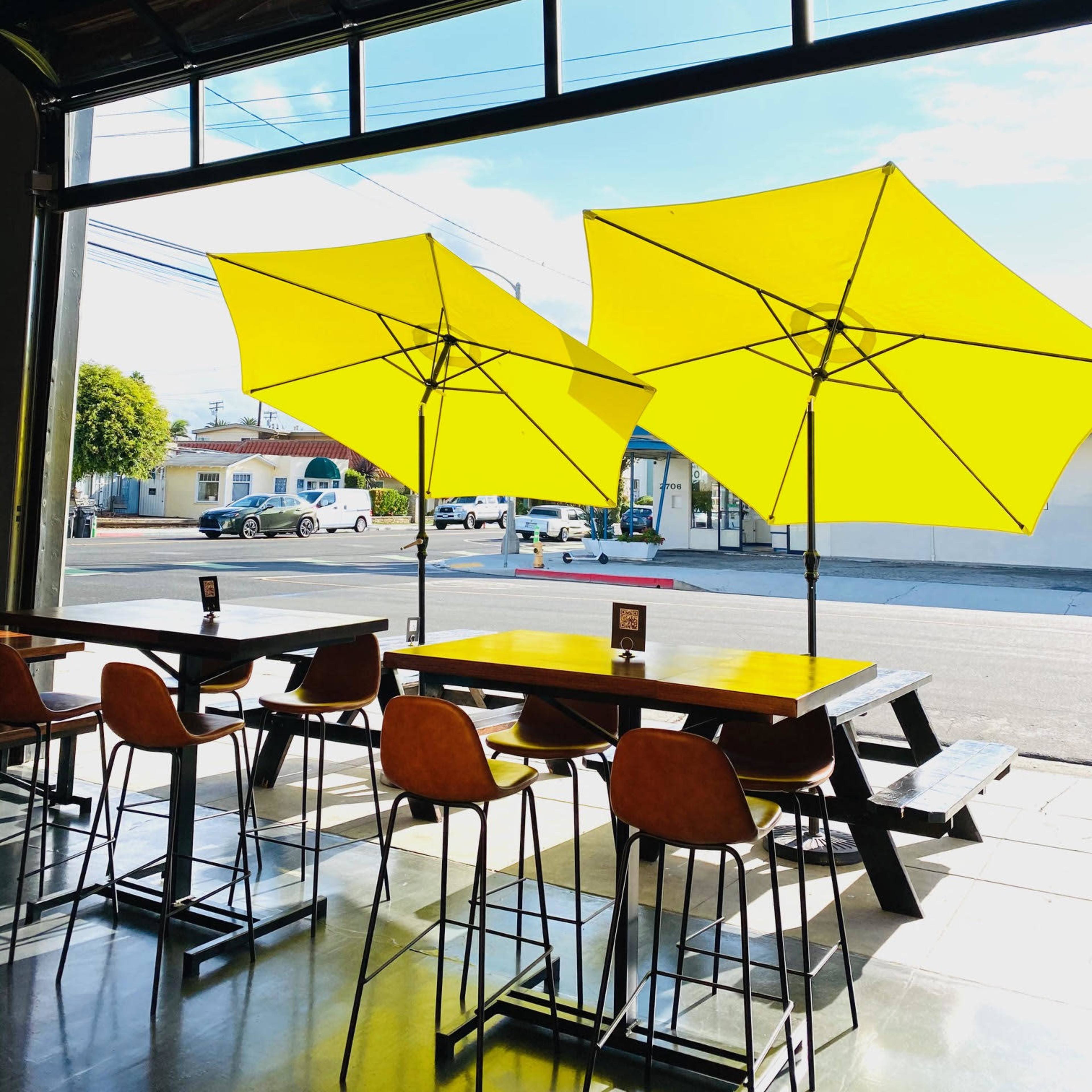 A modern café with yellow umbrellas outside and tall tables arranged inside, illuminated by sunlight.