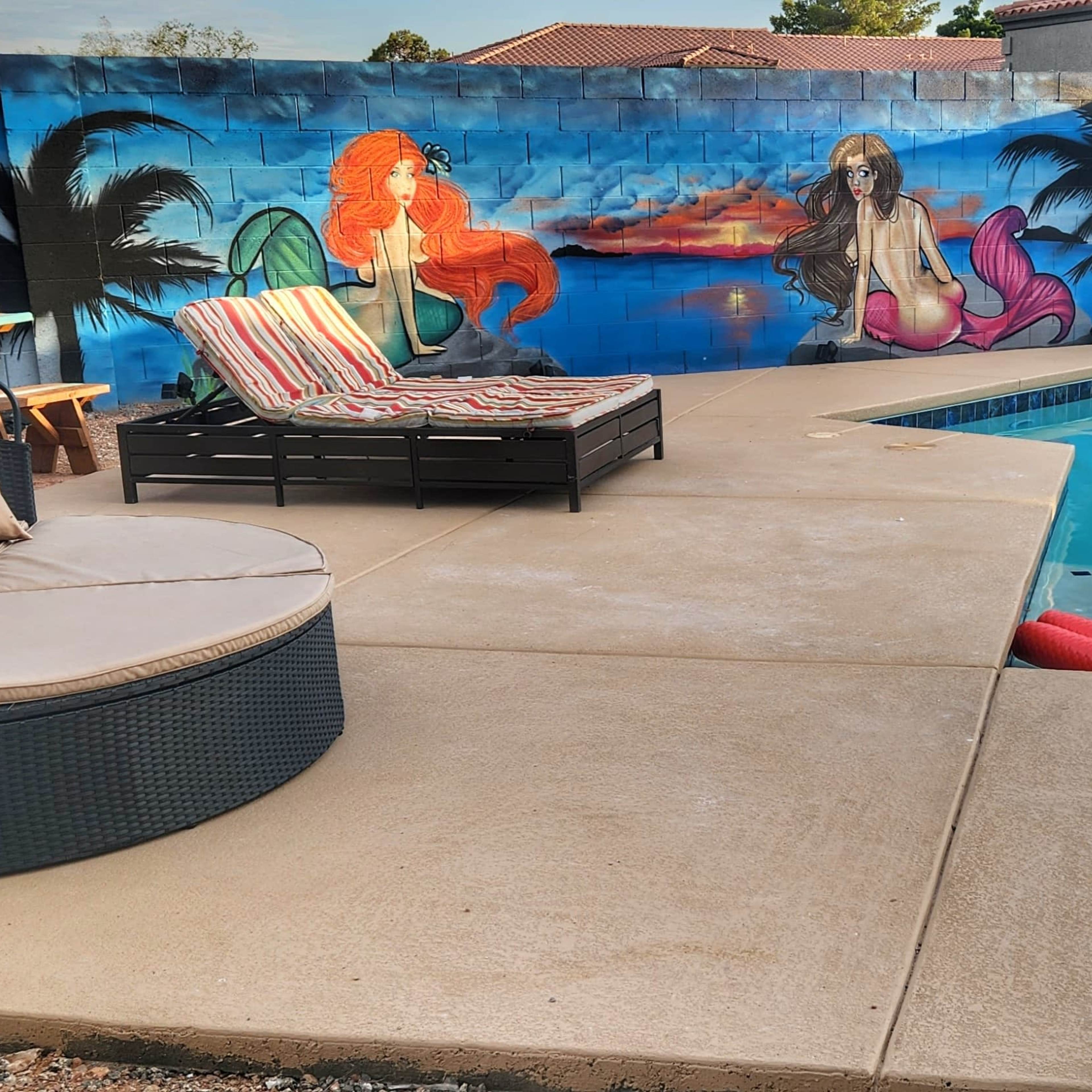 A pool area features a round seating arrangement and lounge chairs beside a colorful mural that includes a mermaid and sea creatures.