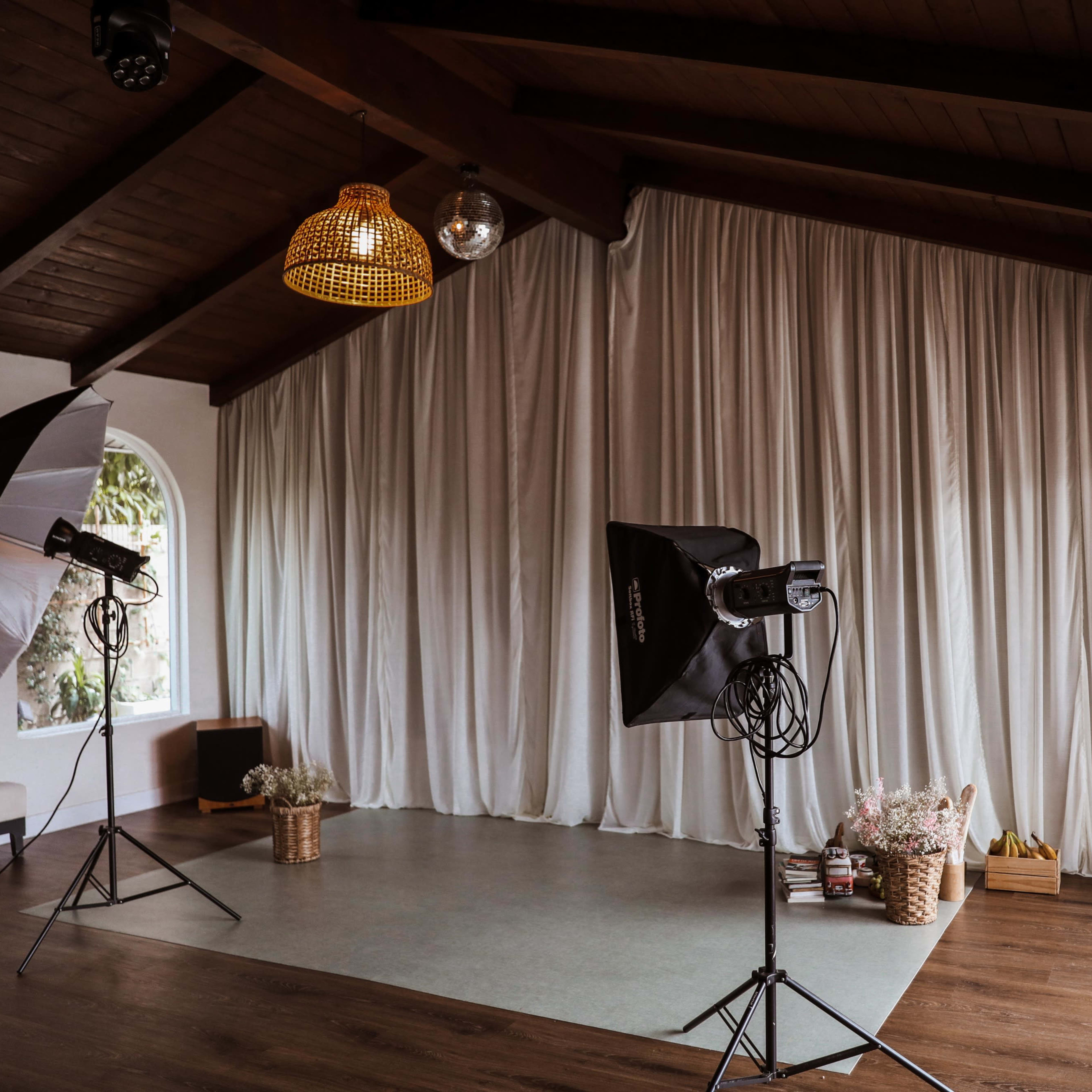 A spacious indoor area with large light modifiers set up on stands and a backdrop of white curtains along one wall.