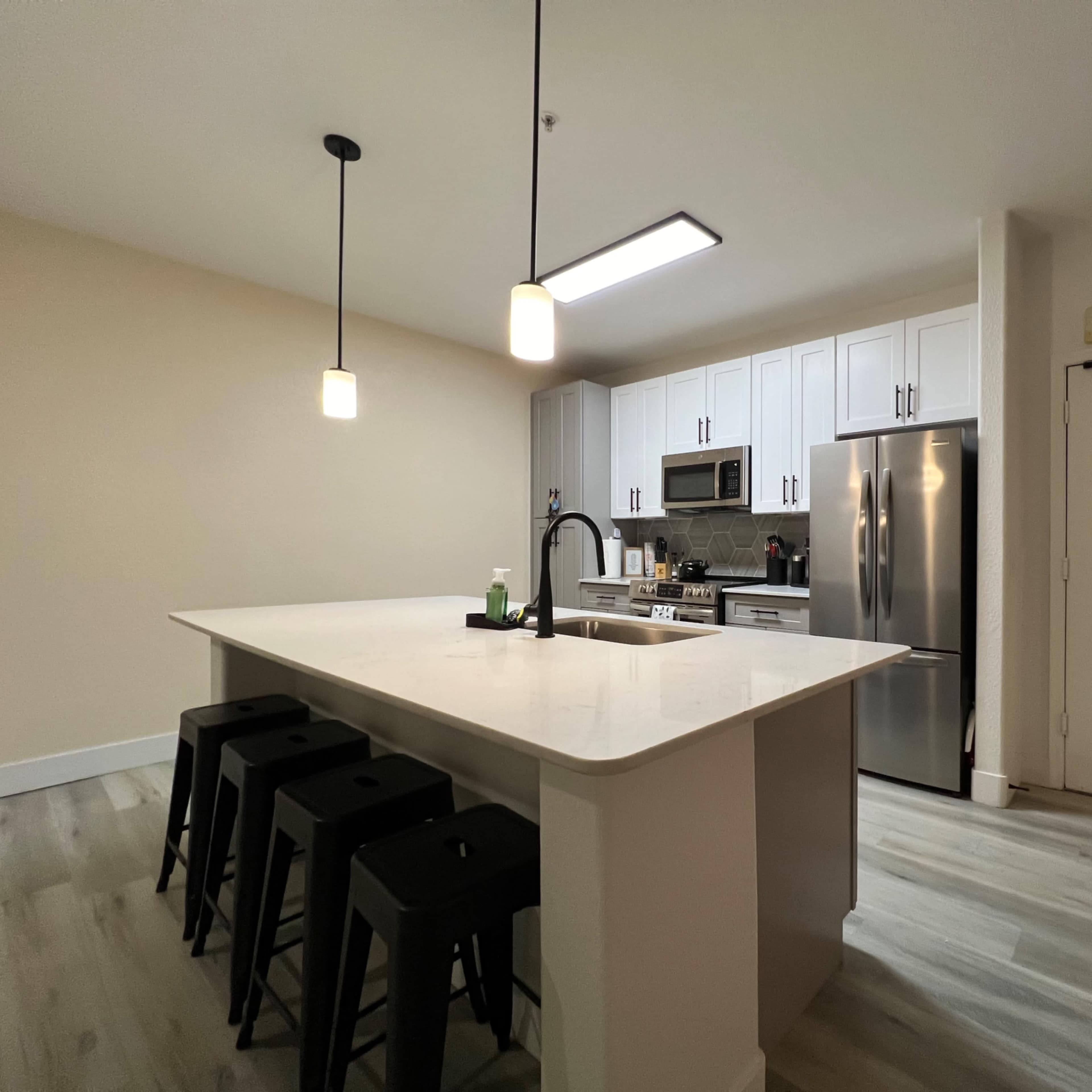 A modern kitchen with white cabinetry, a large island with seating, stainless steel appliances, and a front door visible on the right.