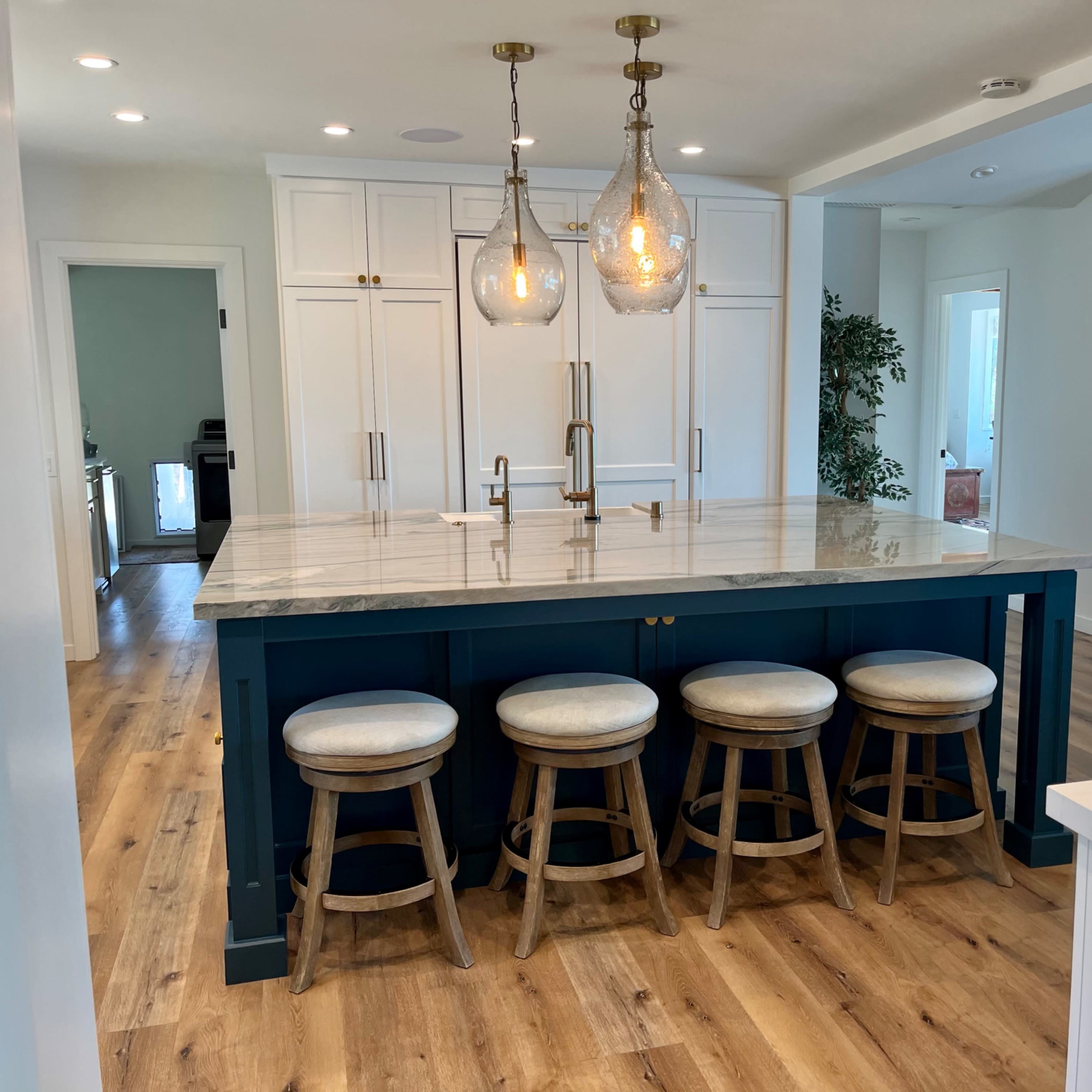 A kitchen features a large marble island with four wooden stools and hanging pendant lights above.