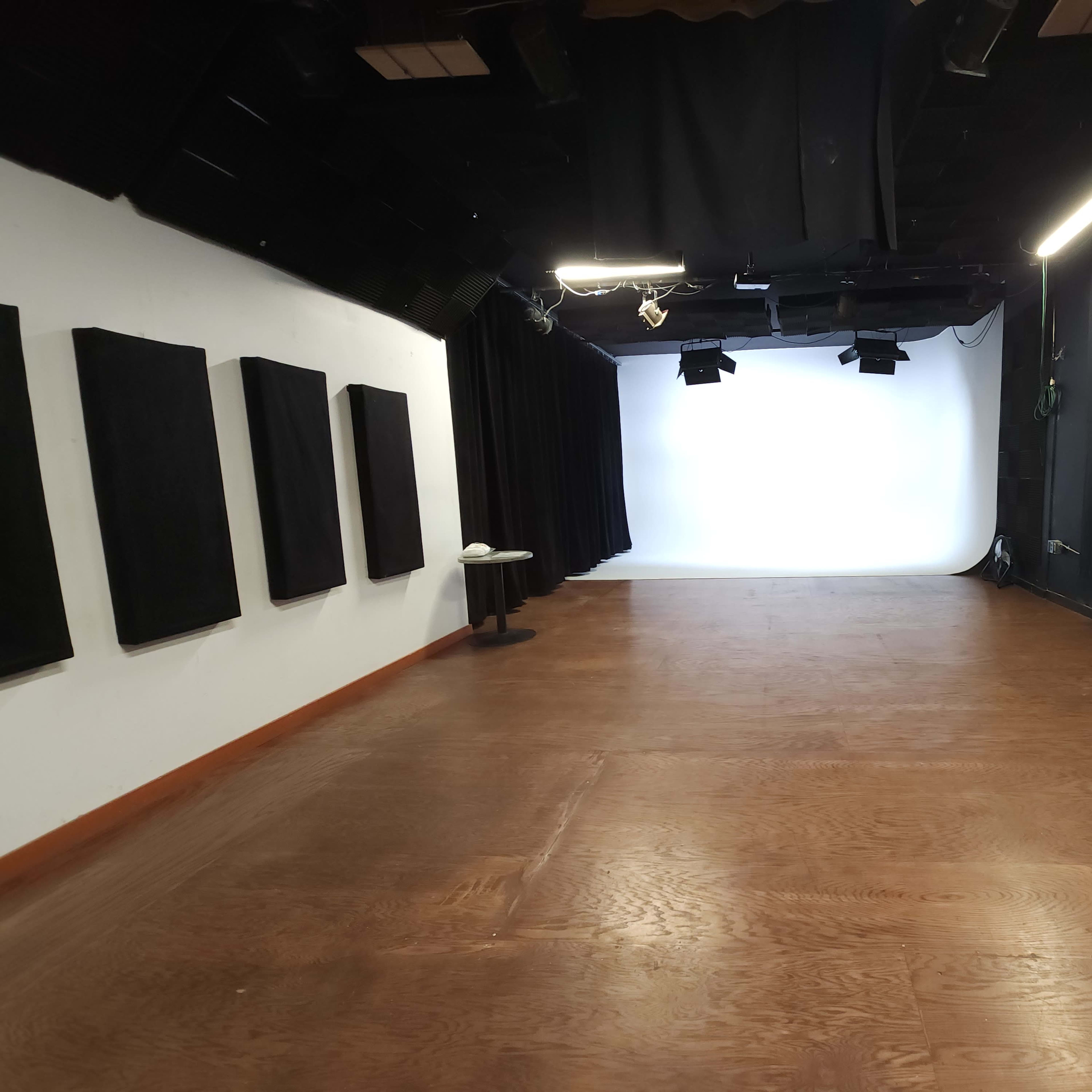 An empty studio space with a white backdrop and black curtains, featuring wooden flooring and two small tables.