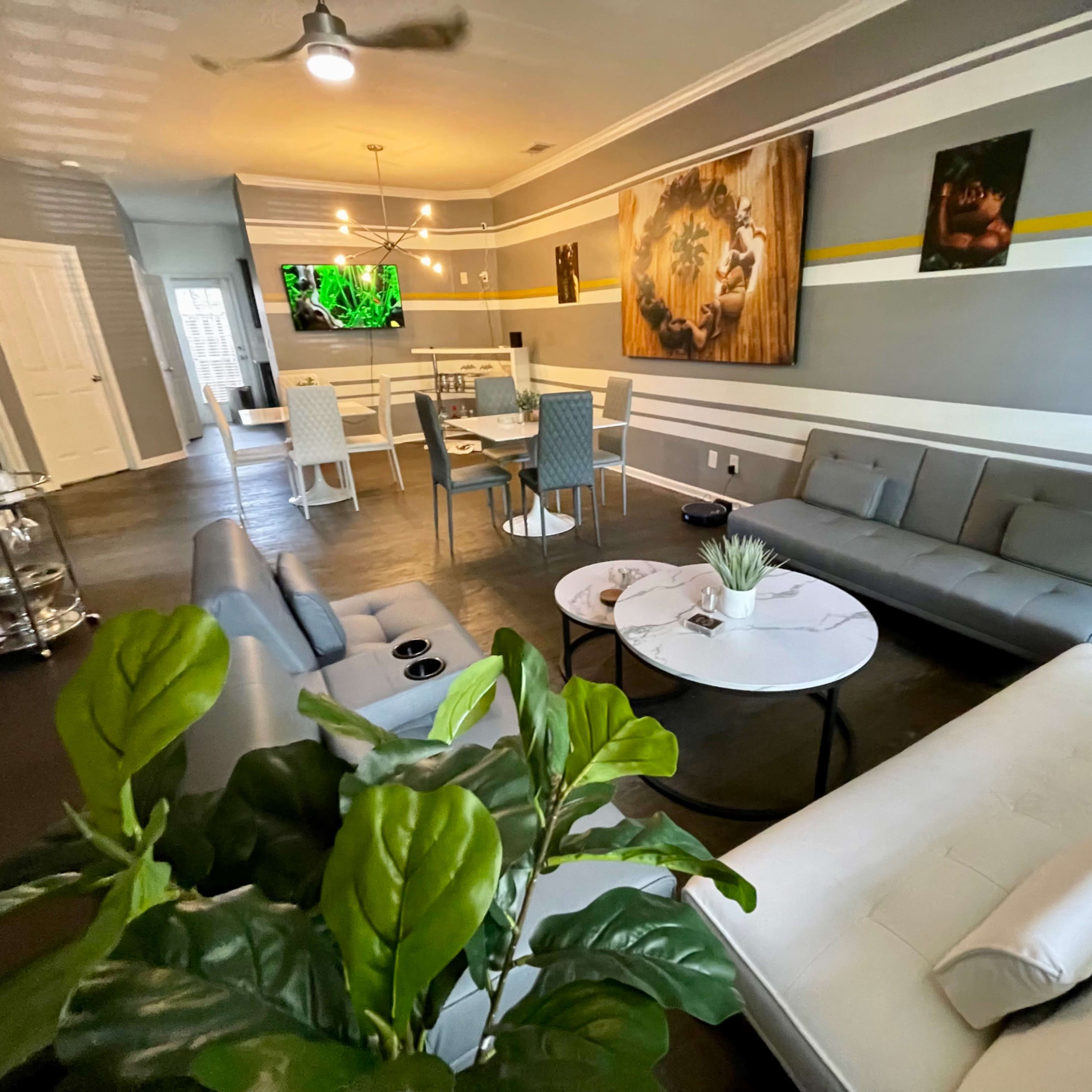 A modern living room with gray walls, a large television mounted on the wall, a circular coffee table, and a mix of seating arrangements including gray sofas and dining chairs.