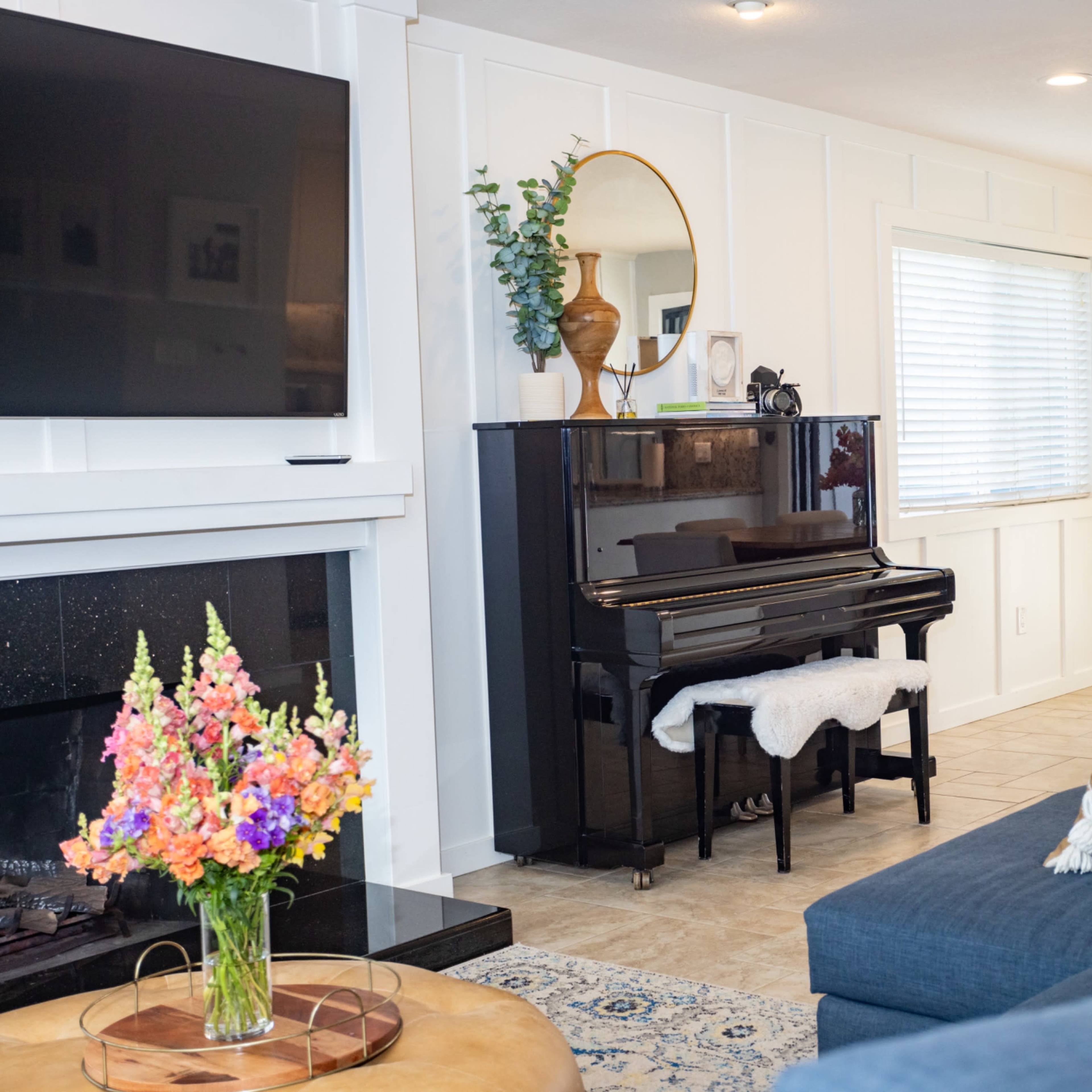 A living room features a black piano next to a television, with a blue sofa and a dining area visible in the background.