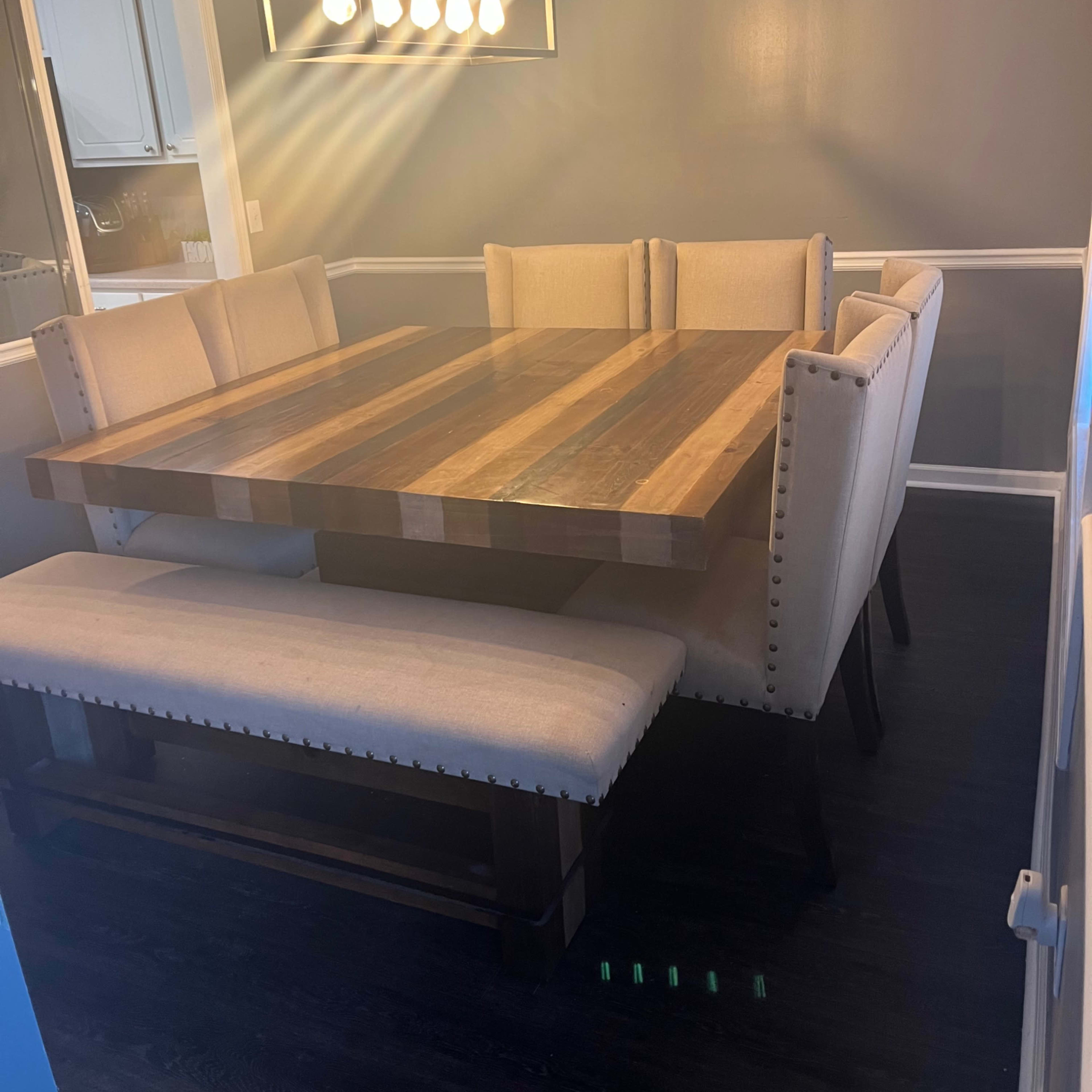 A wooden dining table with a striped design is surrounded by upholstered chairs and a bench in a well-lit dining room.