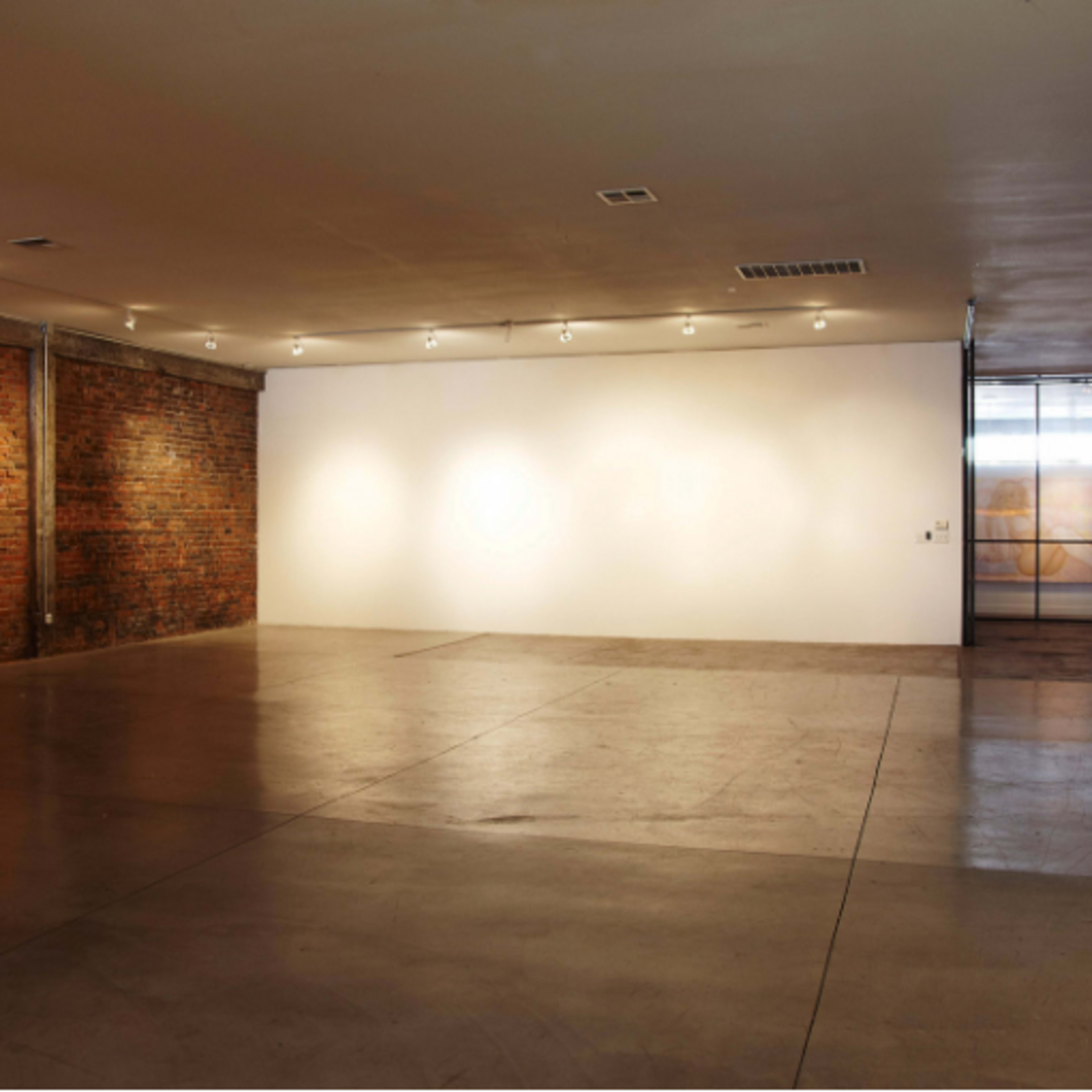An empty art gallery features exposed brick walls and concrete flooring under soft overhead lighting.