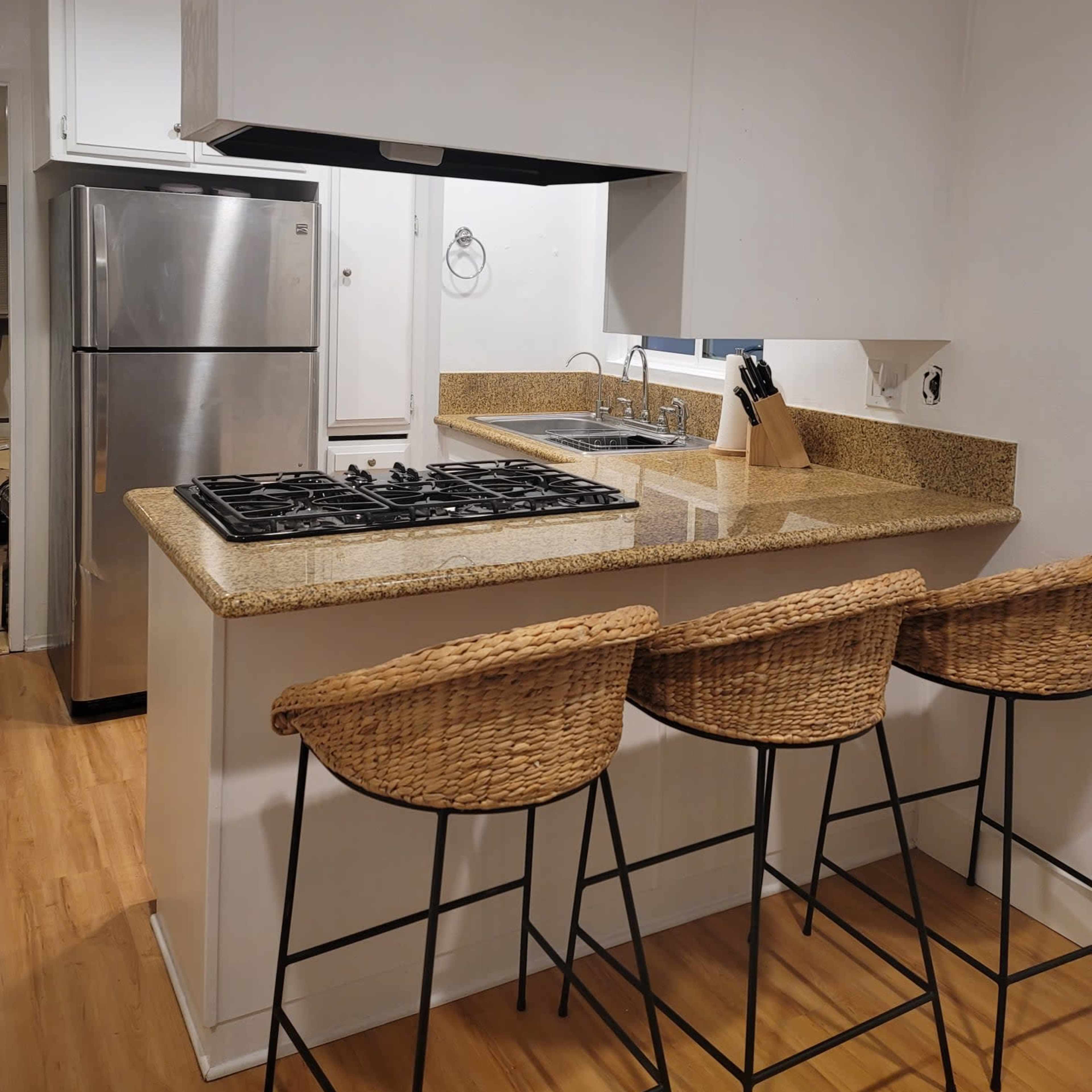 A modern kitchen with a granite countertop, a gas stove, a sink, and three bar stools.