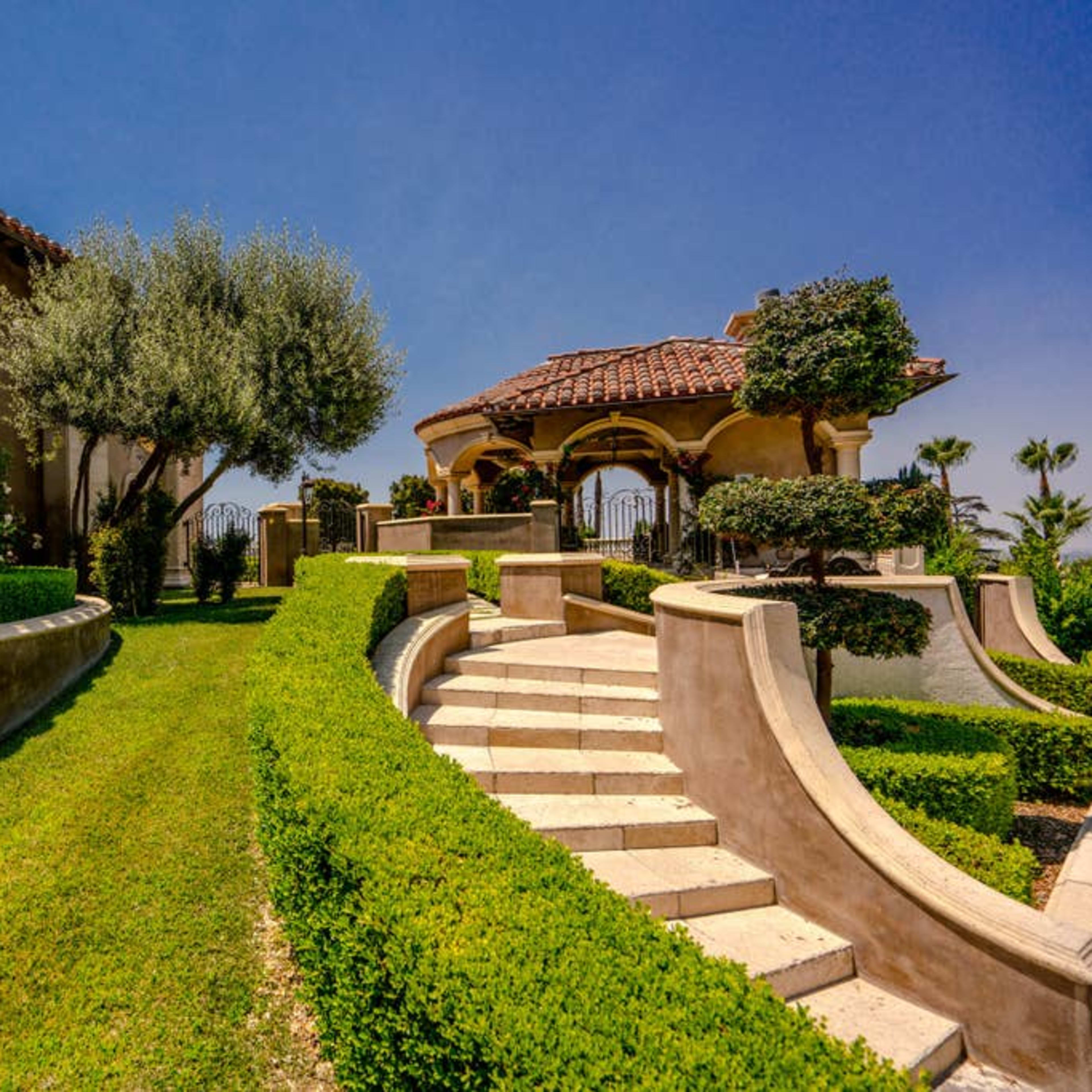 A landscaped garden with a stone staircase leading up to a gazebo and a building with arched windows.