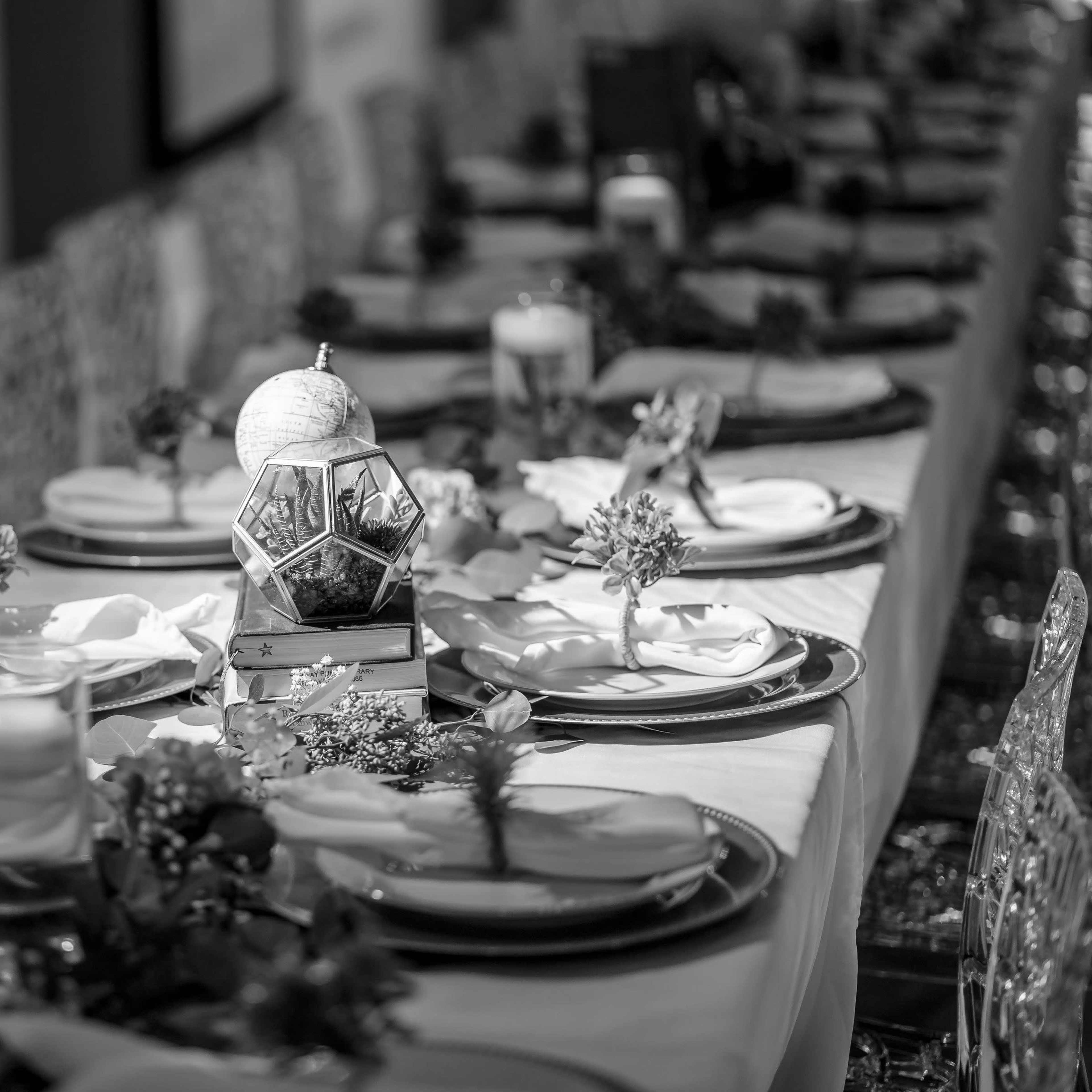 A long dining table is elegantly set with plates, utensils, and decorative arrangements, including a geometric centerpiece.