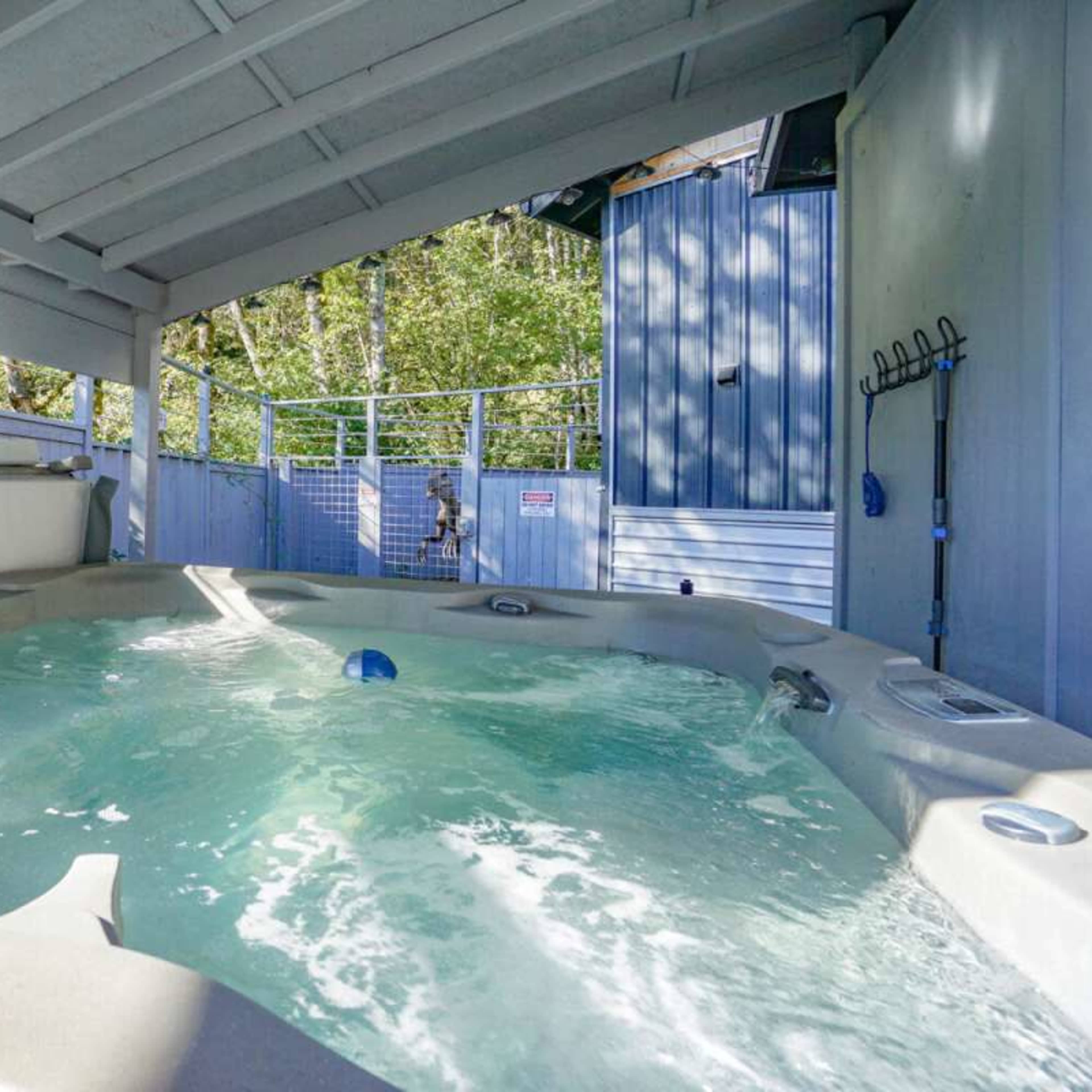 A hot tub under a roof with a view of a fenced area and trees in the background.