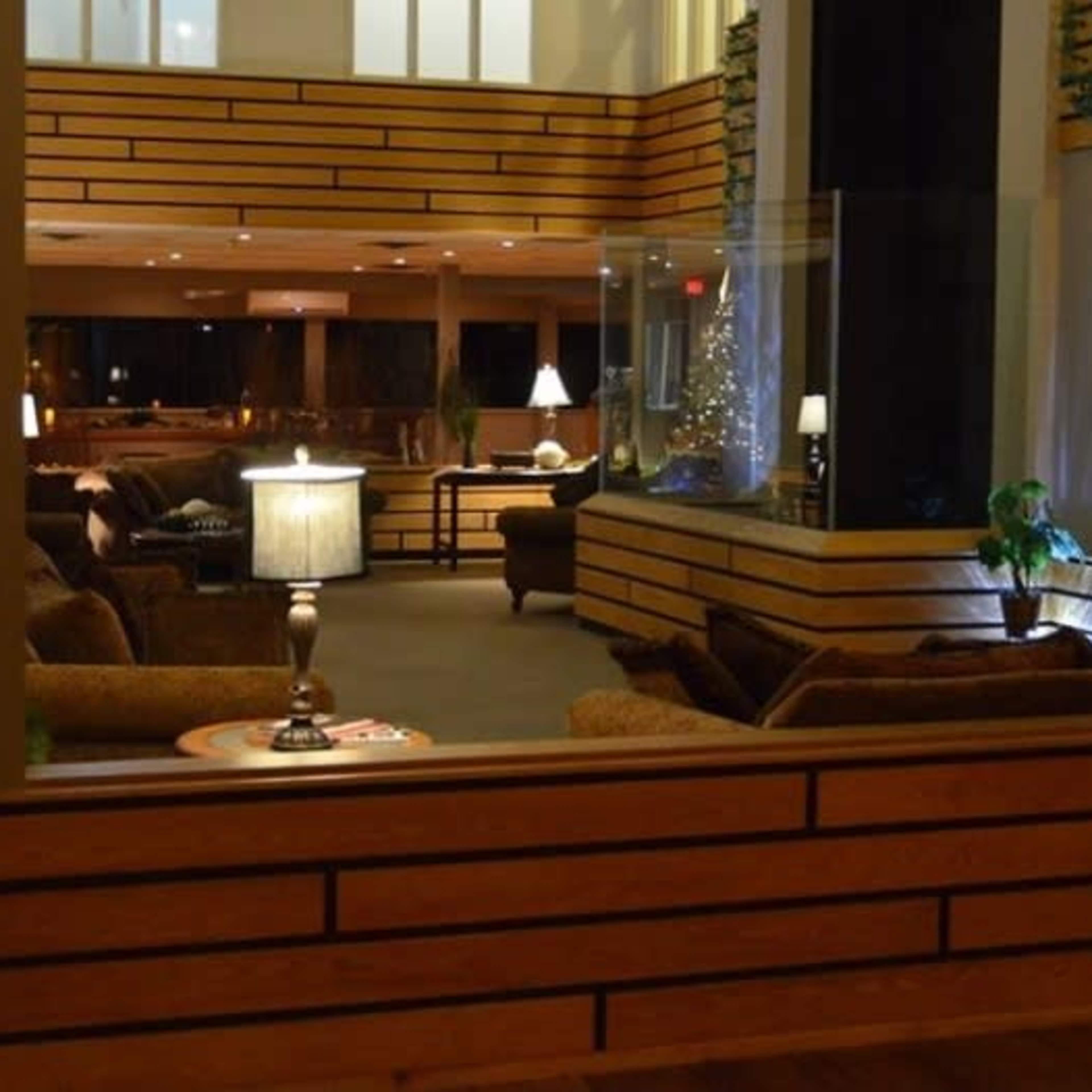 A spacious interior lounge area with wooden flooring, comfortable seating, decorative lamps, and large windows allowing natural light.