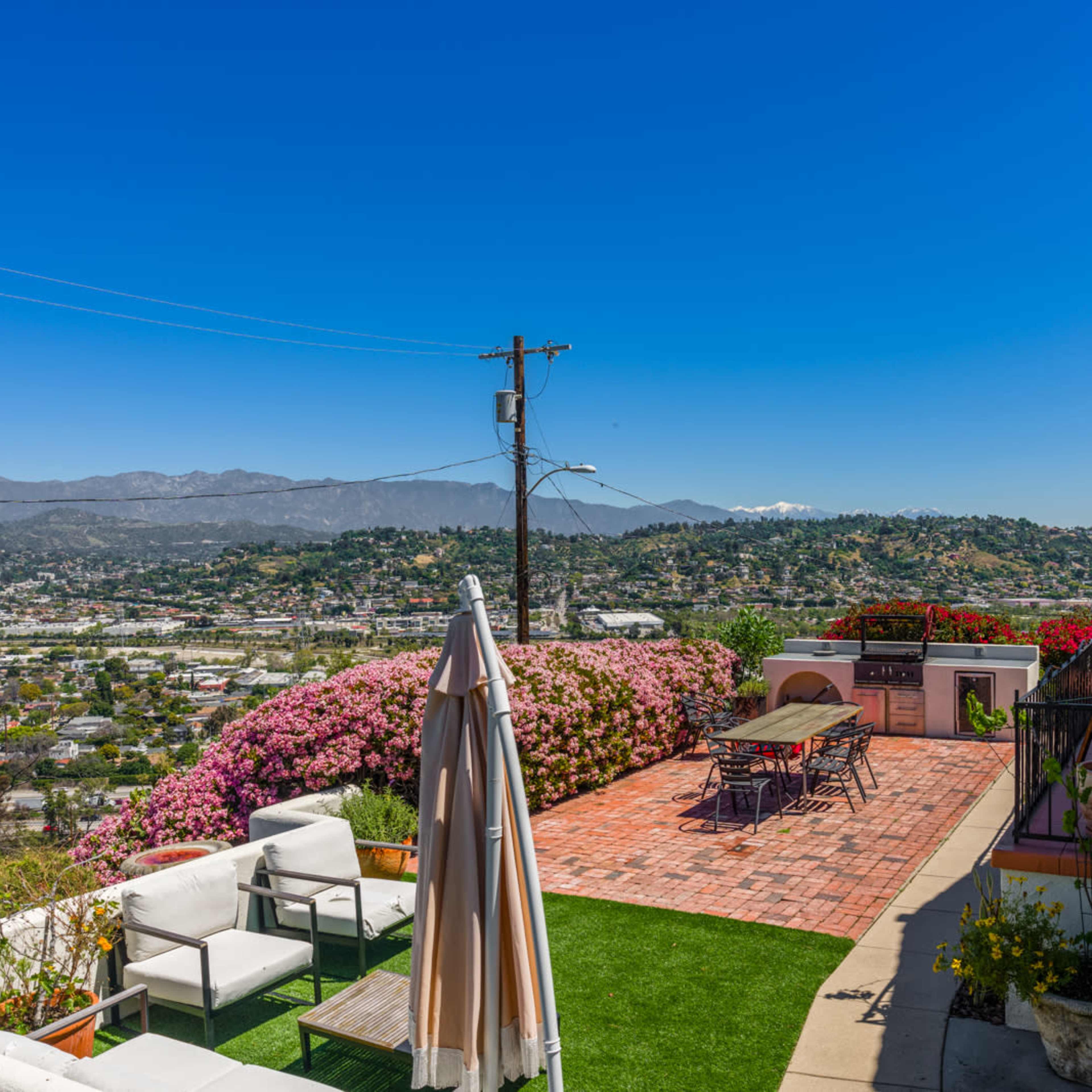 A patio with seating overlooks a valley filled with houses and mountains in the distance.
