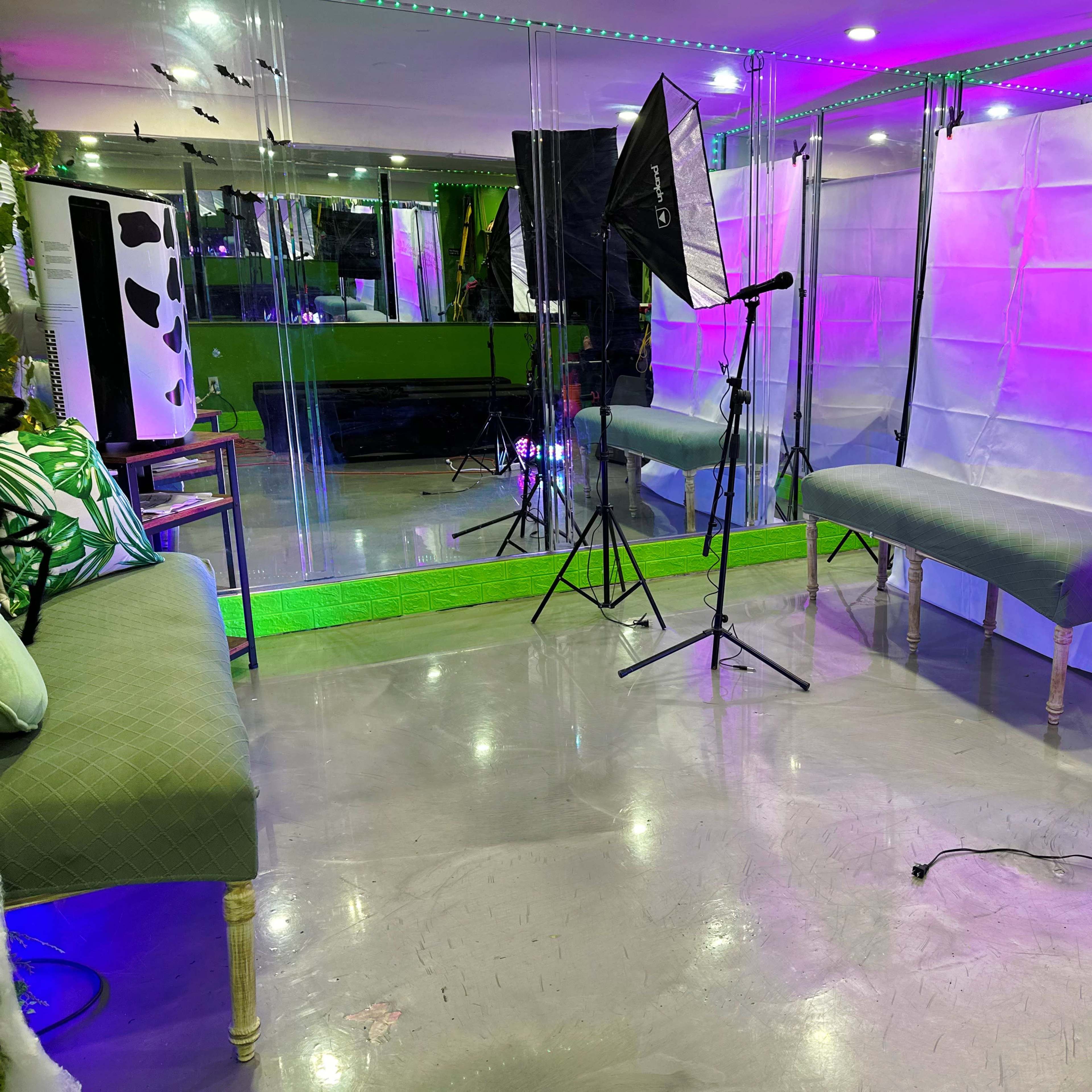 A photography studio setup with two light umbrellas, a microphone on a stand, and mirrored walls reflecting green and purple lighting.