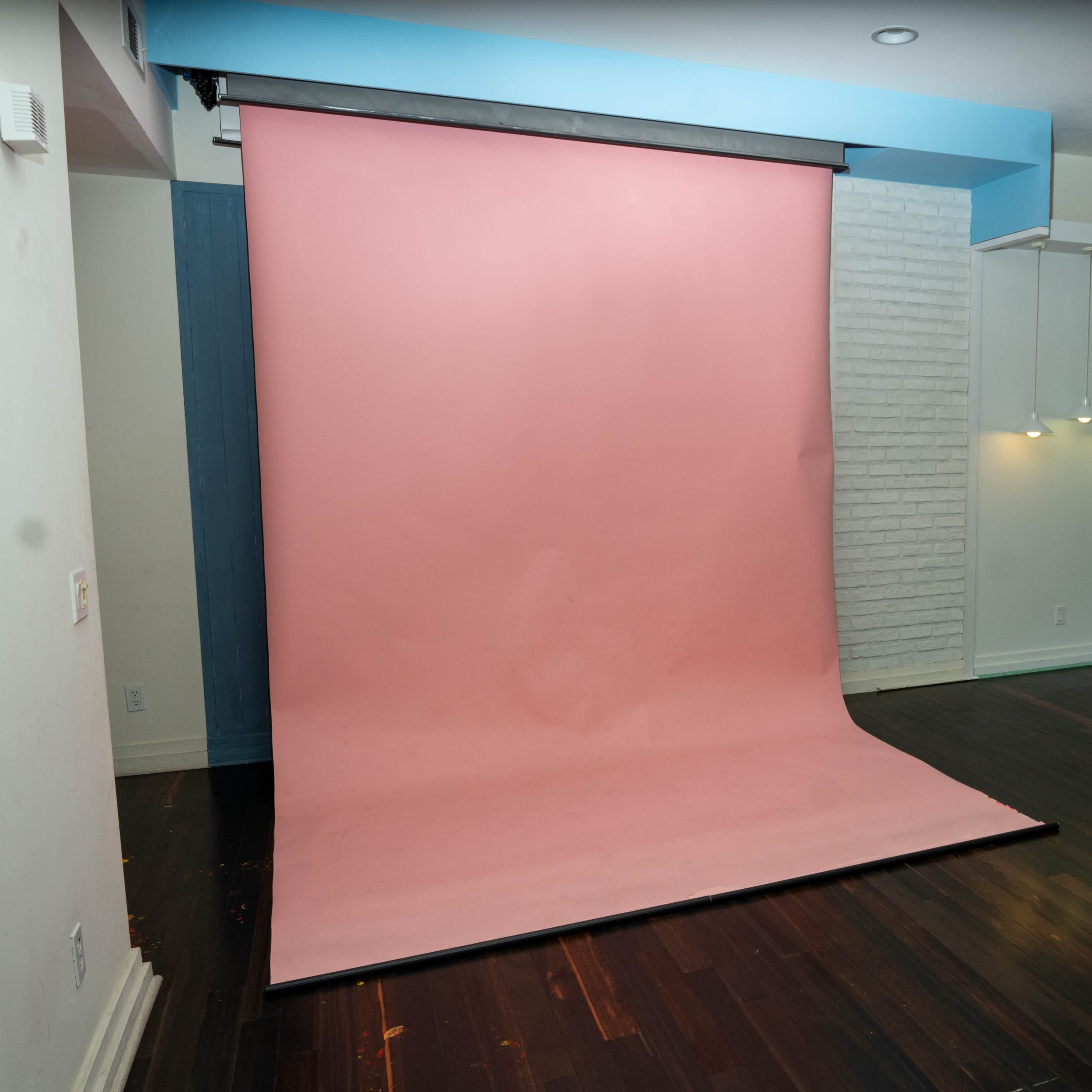 A spacious room with a pink backdrop, wooden flooring, and large windows allowing natural light.