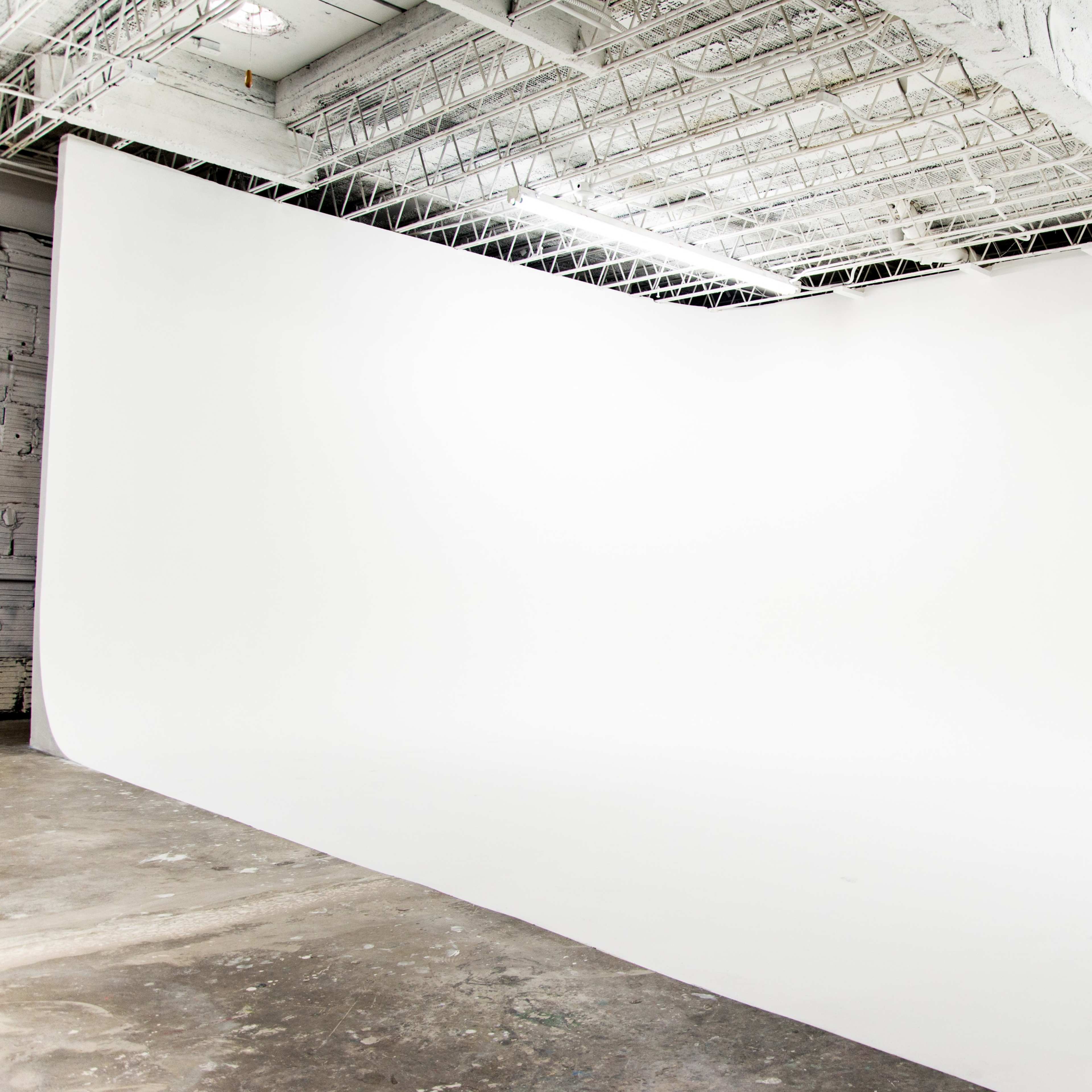 An empty photo studio with a large, white backdrop and a concrete floor.