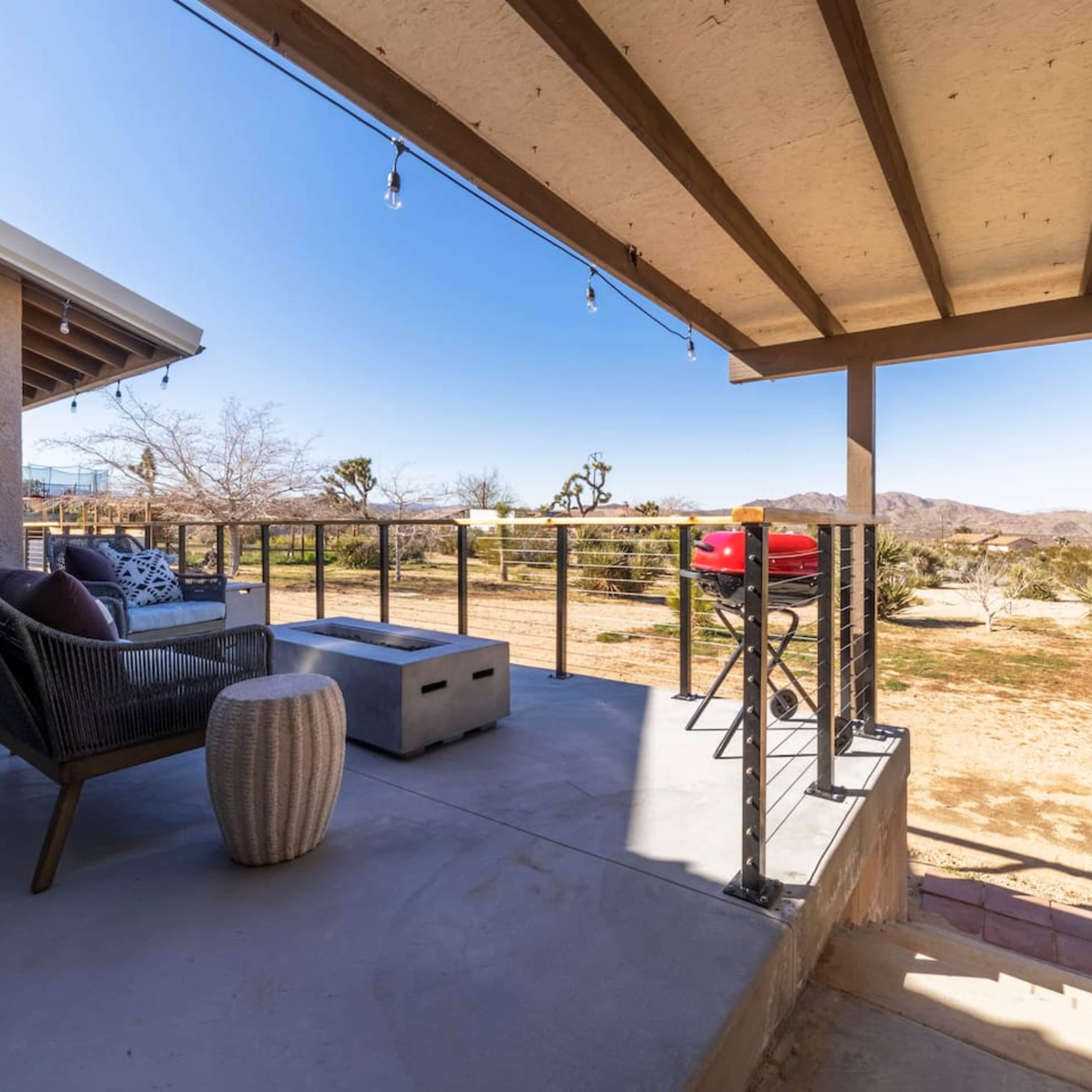 A shaded outdoor patio features a seating area with a modern chair, a small side table, and a view of the desert landscape.