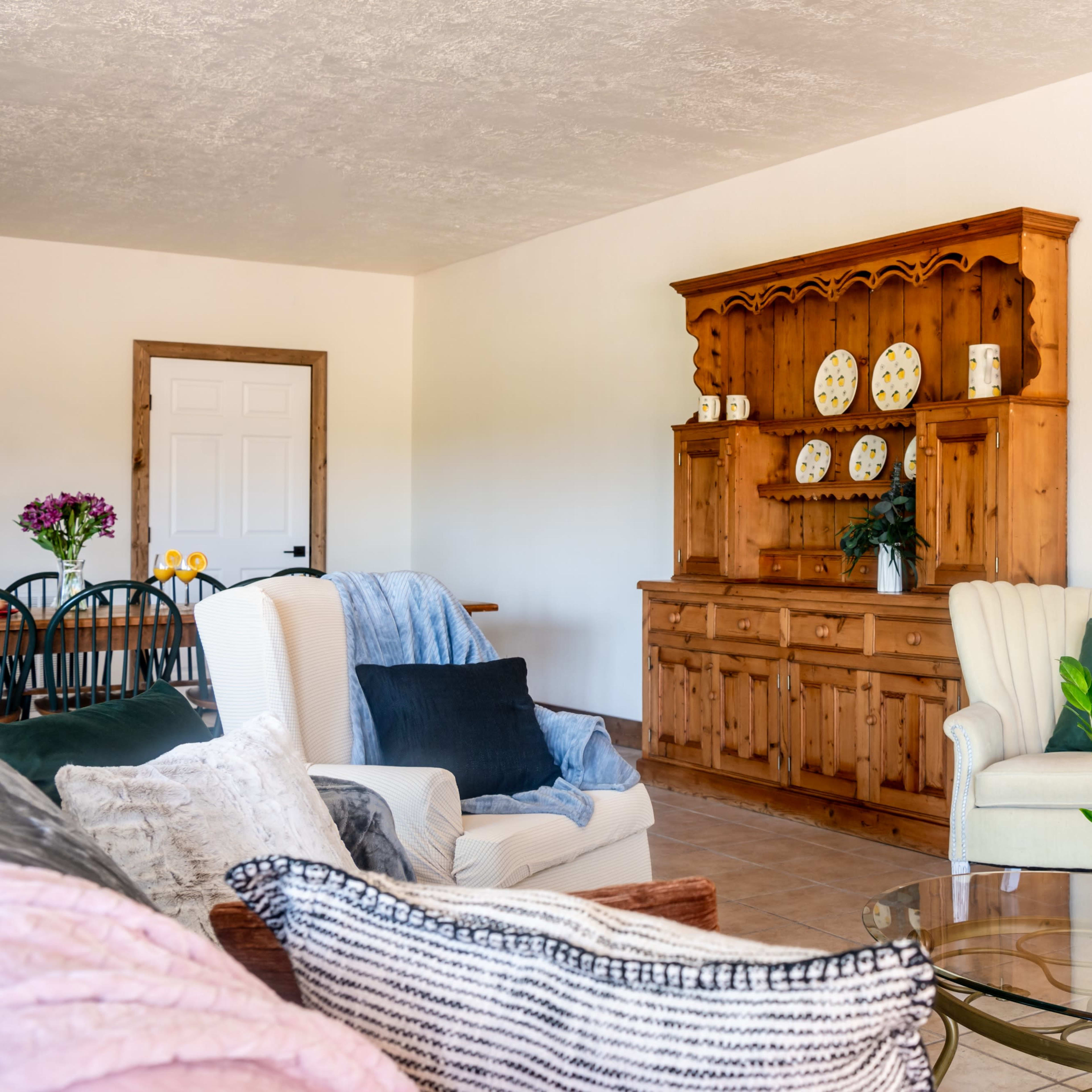 A living room with wooden furniture, including a cabinet and armchairs, a coffee table, and a television mounted on the wall.