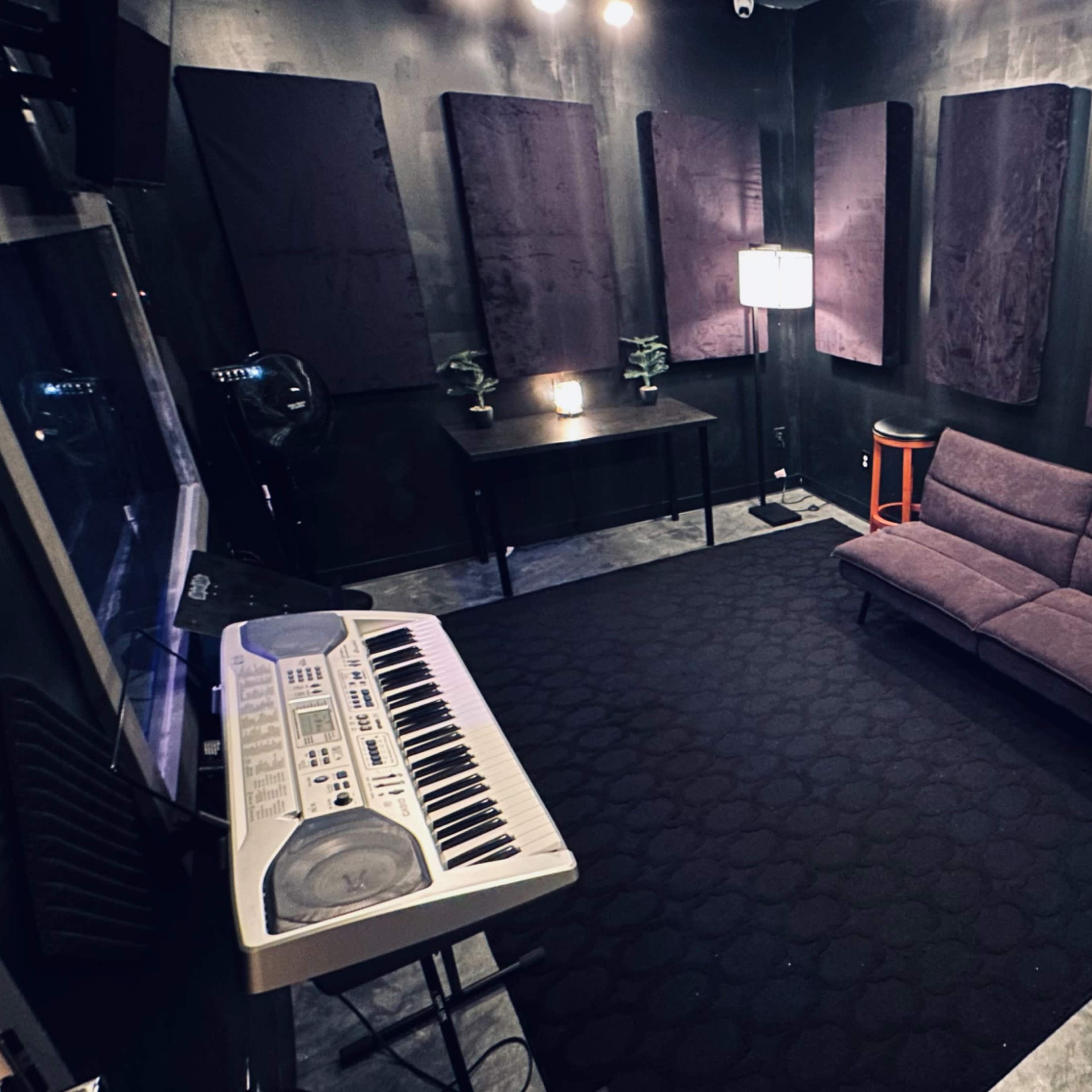 A soundproof room featuring a keyboard, a dark couch, and padded walls.