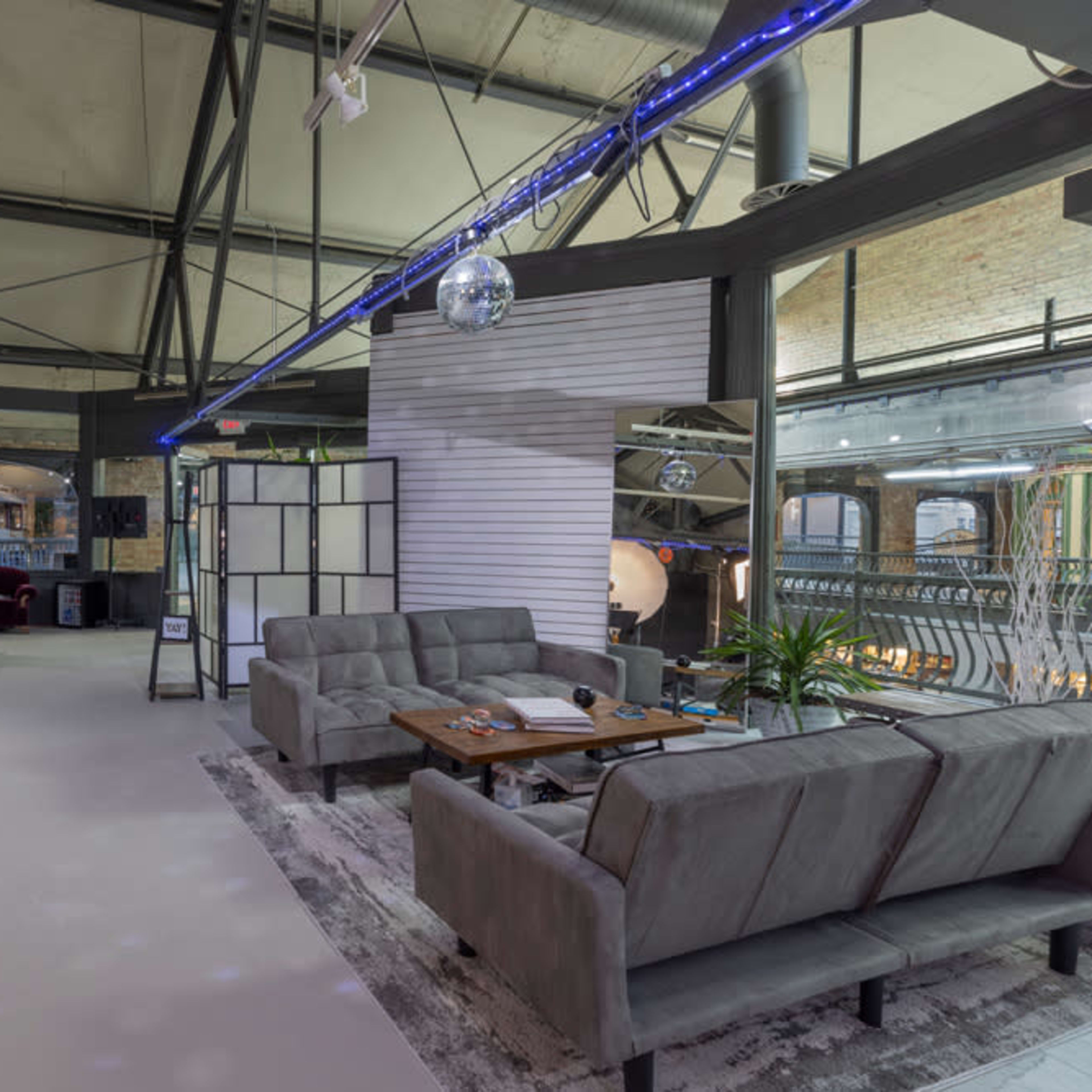 A modern open space with gray sofas, a dining area with a table, and large windows allowing natural light in.