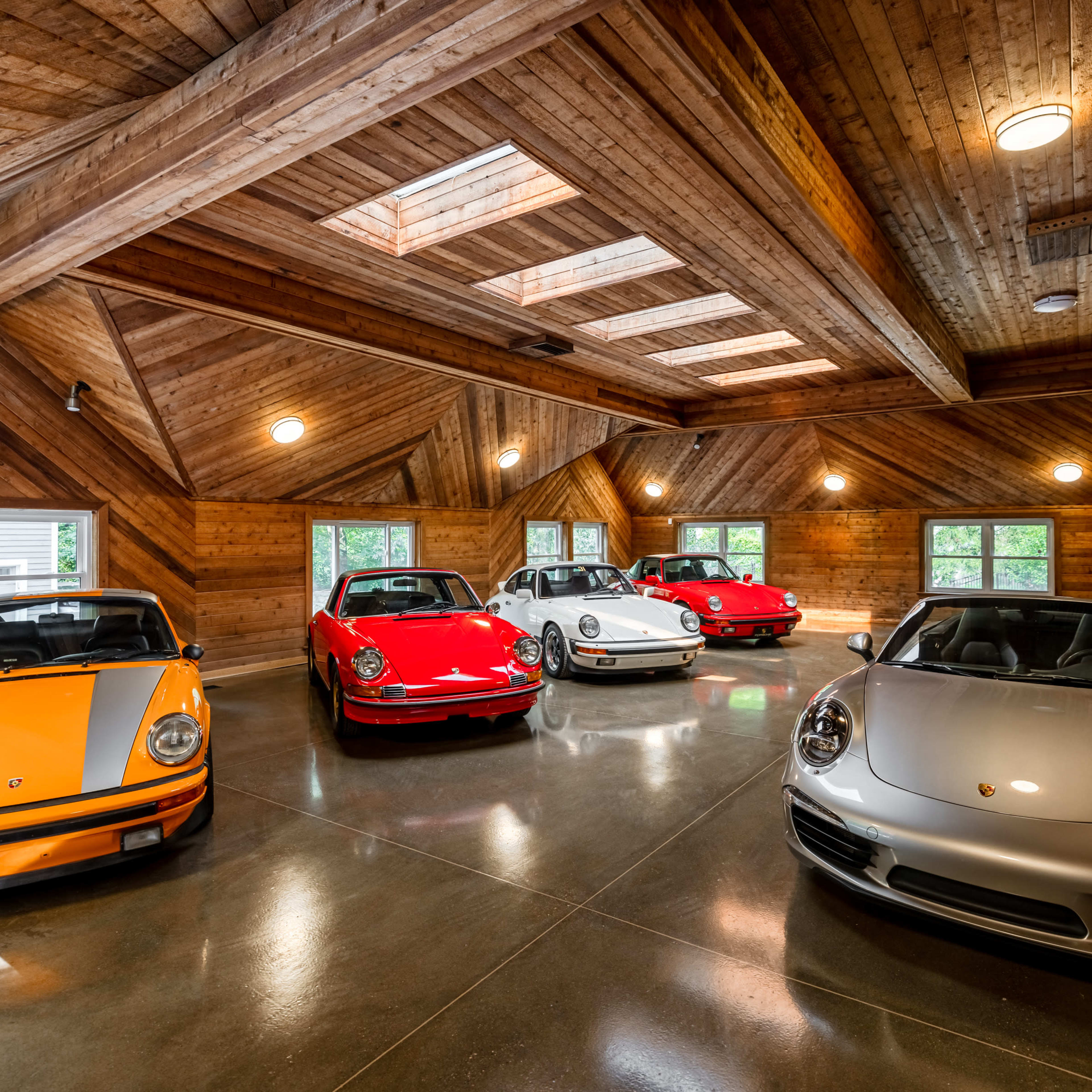 A garage with five classic and modern Porsche cars arranged in a wooden-paneled space with skylights.