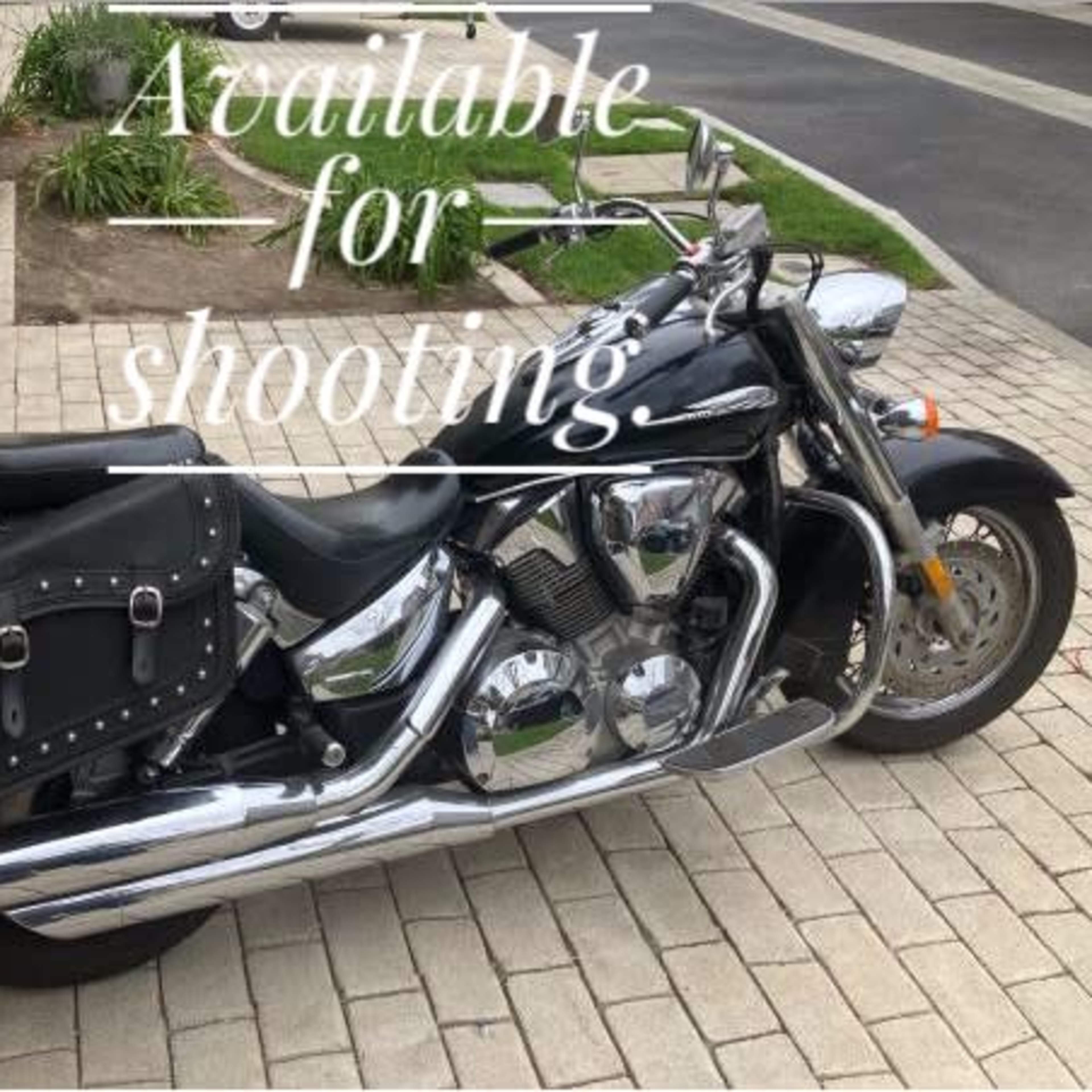 A black motorcycle with a leather saddlebag is parked on a paved driveway.