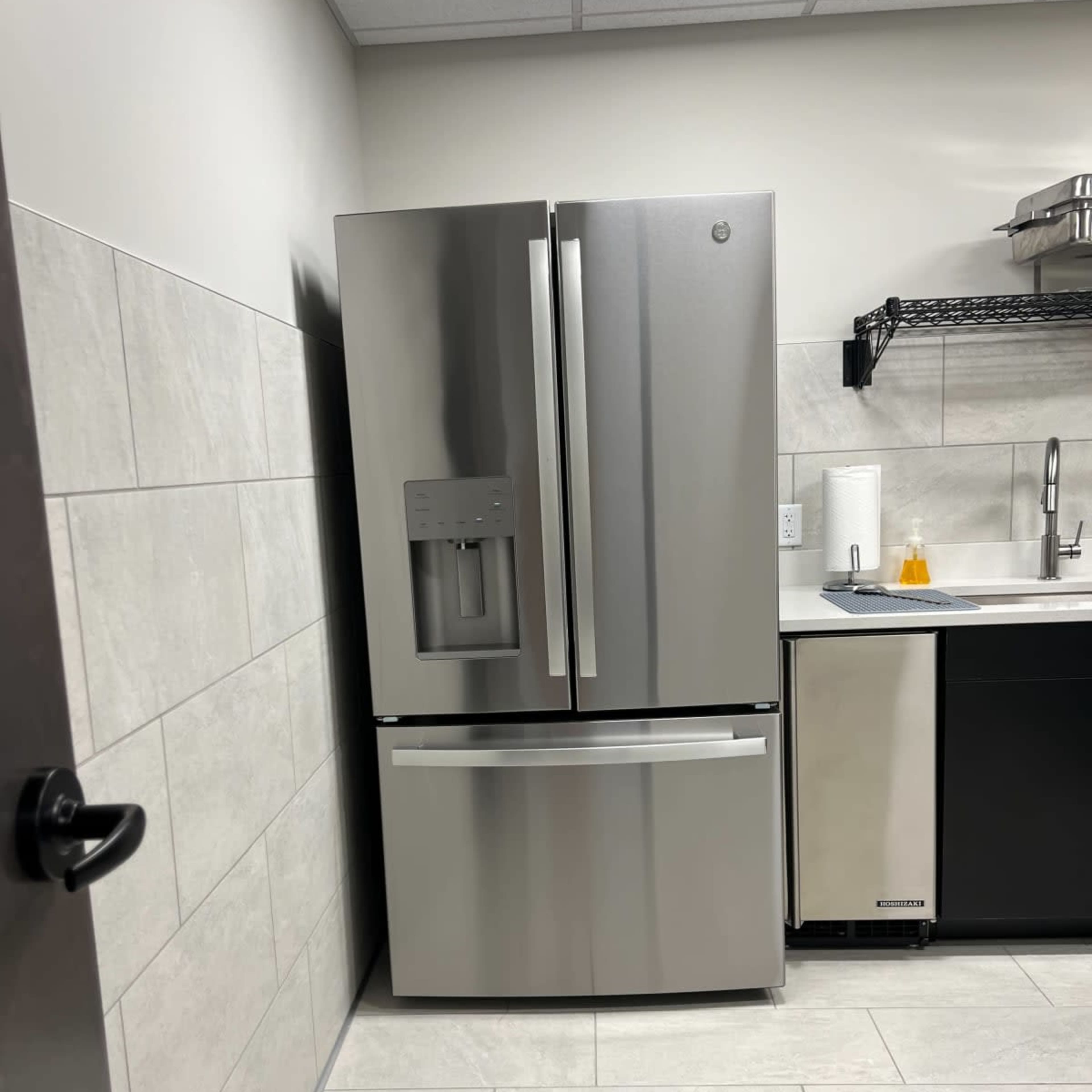 A stainless steel refrigerator standing next to a sink in a modern kitchen.