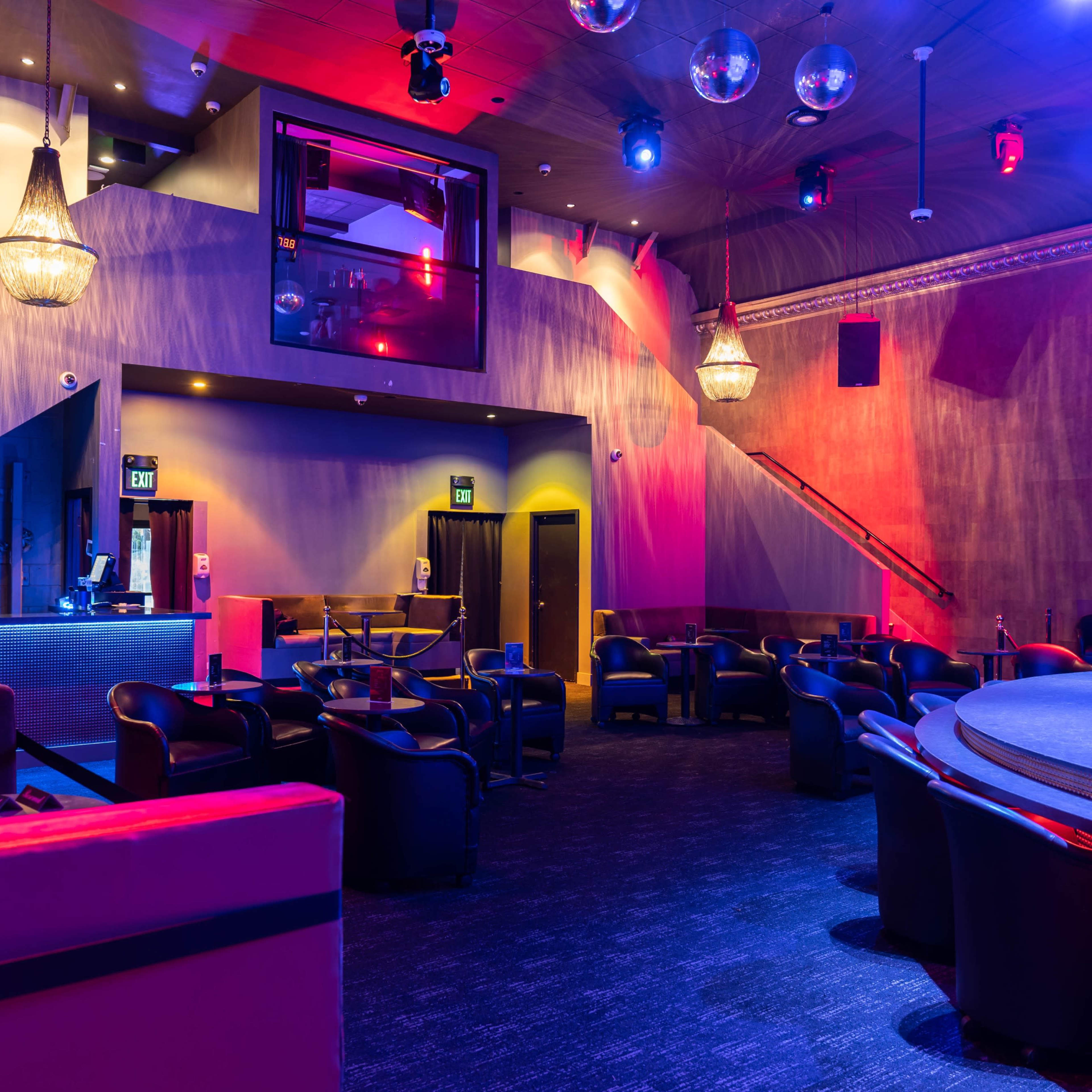 A dimly lit lounge area with seating, a stage, and decorative lighting fixtures.
