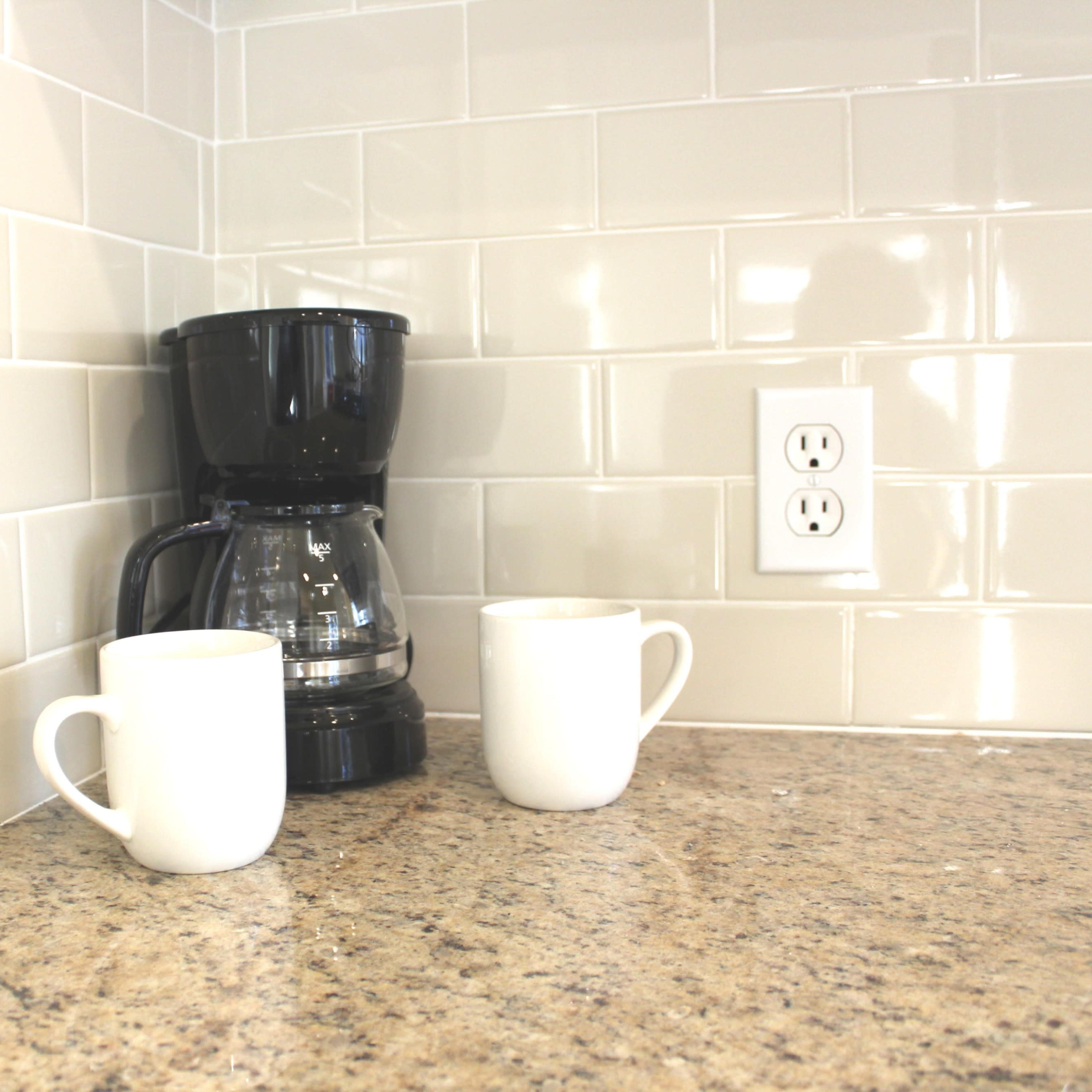 A coffee maker sits on a granite countertop next to two white mugs and an electrical outlet.