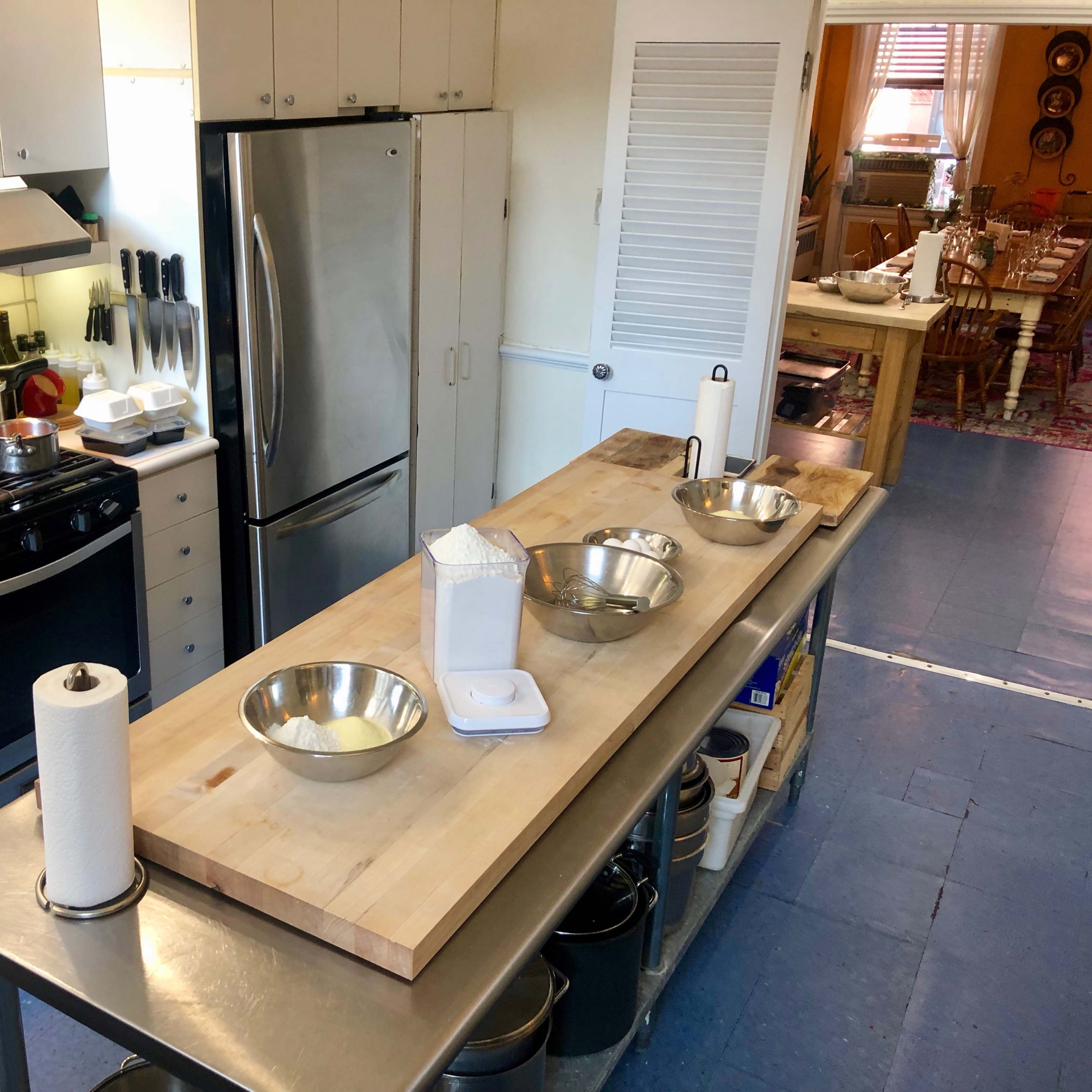 A kitchen with stainless steel appliances, a central wooden prep table, and bowls arranged on the table, ready for cooking.