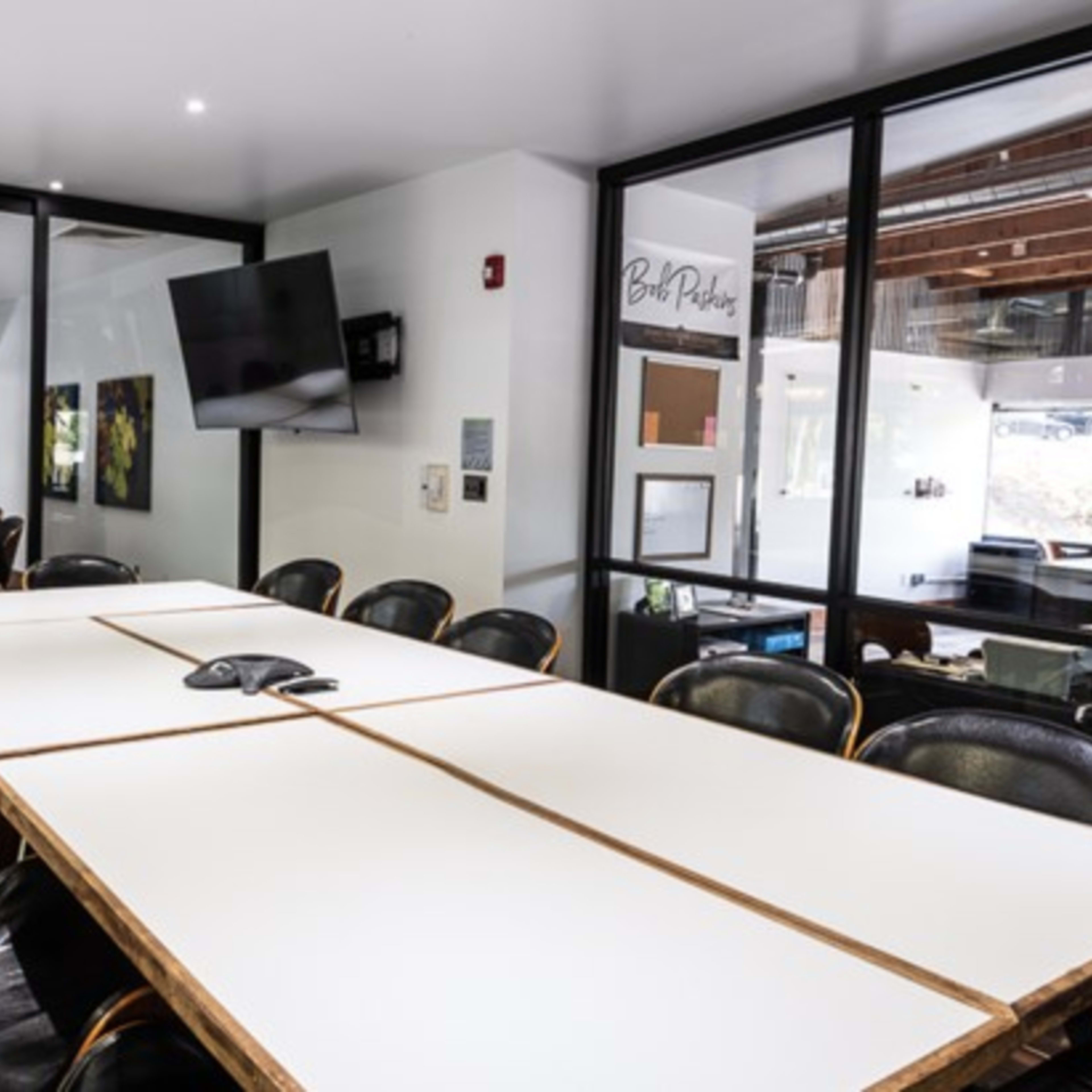 A modern conference room with a long wooden table surrounded by stylish black chairs and a large wall-mounted screen.