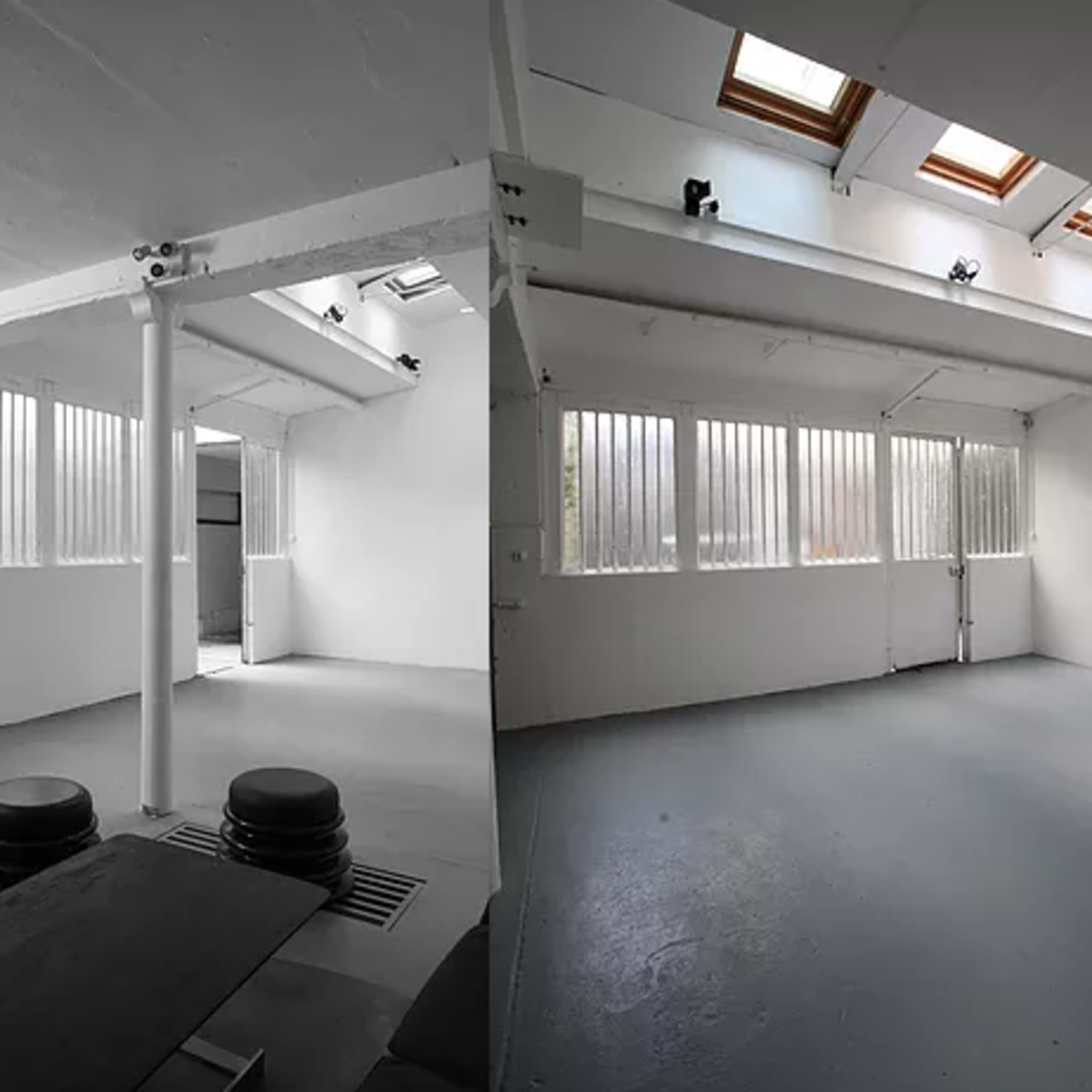 A spacious, bright studio with high ceilings, skylights, and large windows, featuring minimal furnishings and a gray floor.
