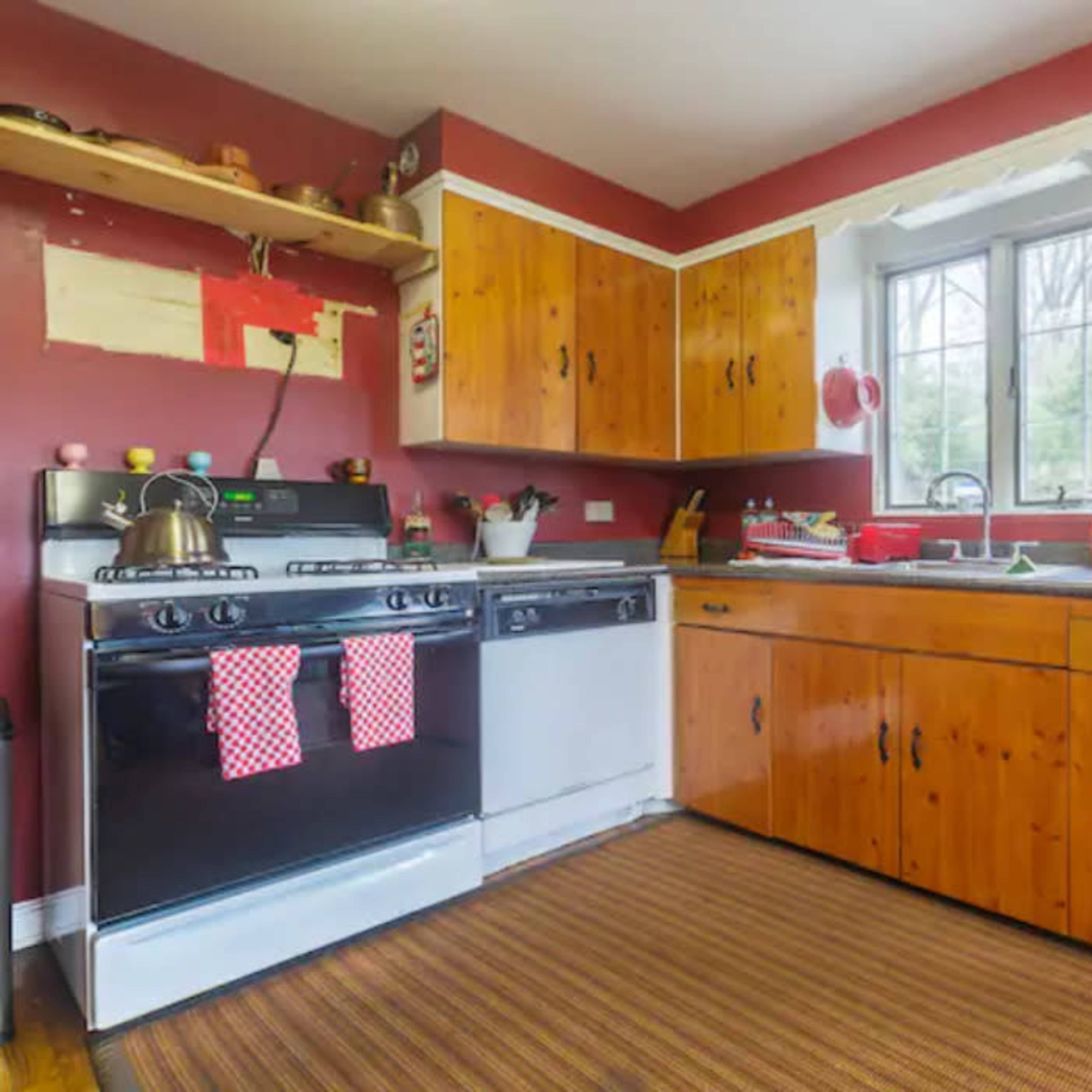 The kitchen features wooden cabinets with a red accent wall, a gas stove, a dishwasher, and a countertop with various kitchen items.