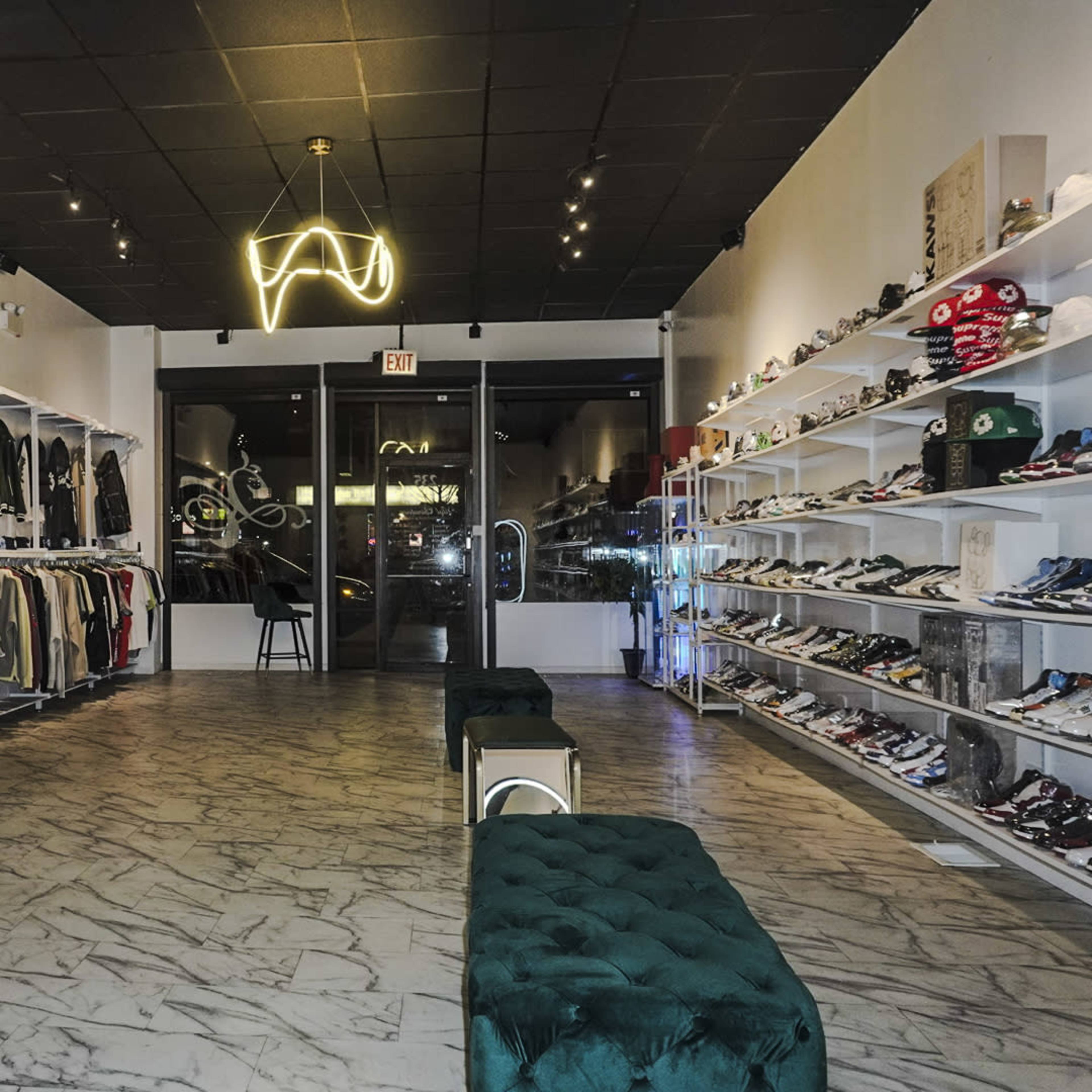 The interior of a retail store features clothing racks on the left and shelves displaying sneakers on the right, with a modern lighting fixture overhead.