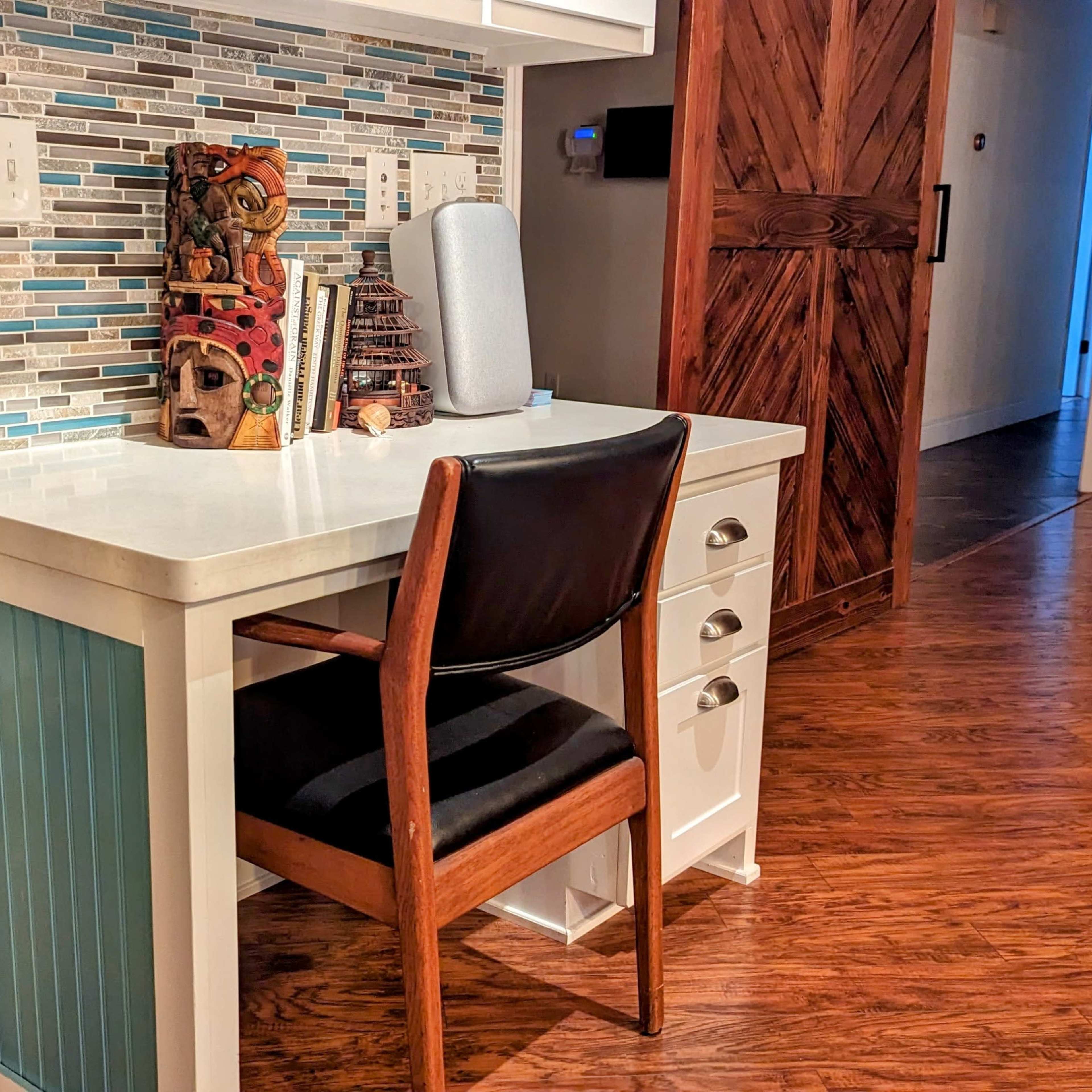 A small desk with a black chair is positioned against a wall featuring a decorative backsplash of blue and gray tiles.