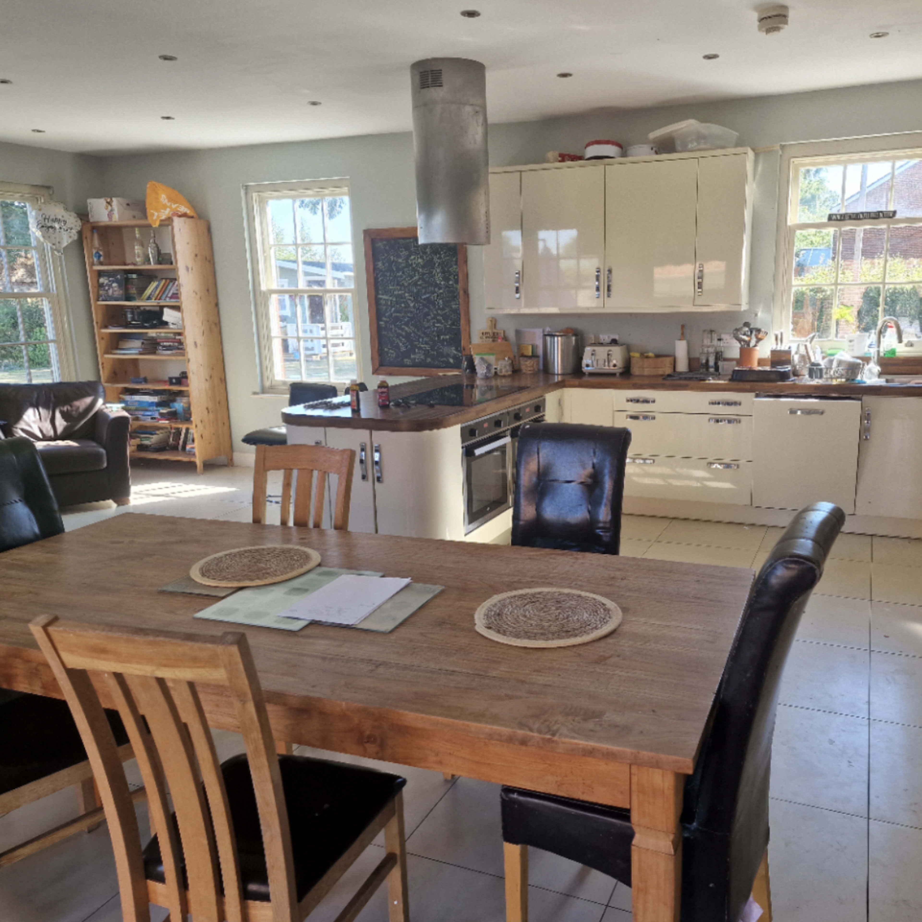 A spacious kitchen features a large wooden dining table surrounded by chairs, with a modern stove and cabinets lining the walls.