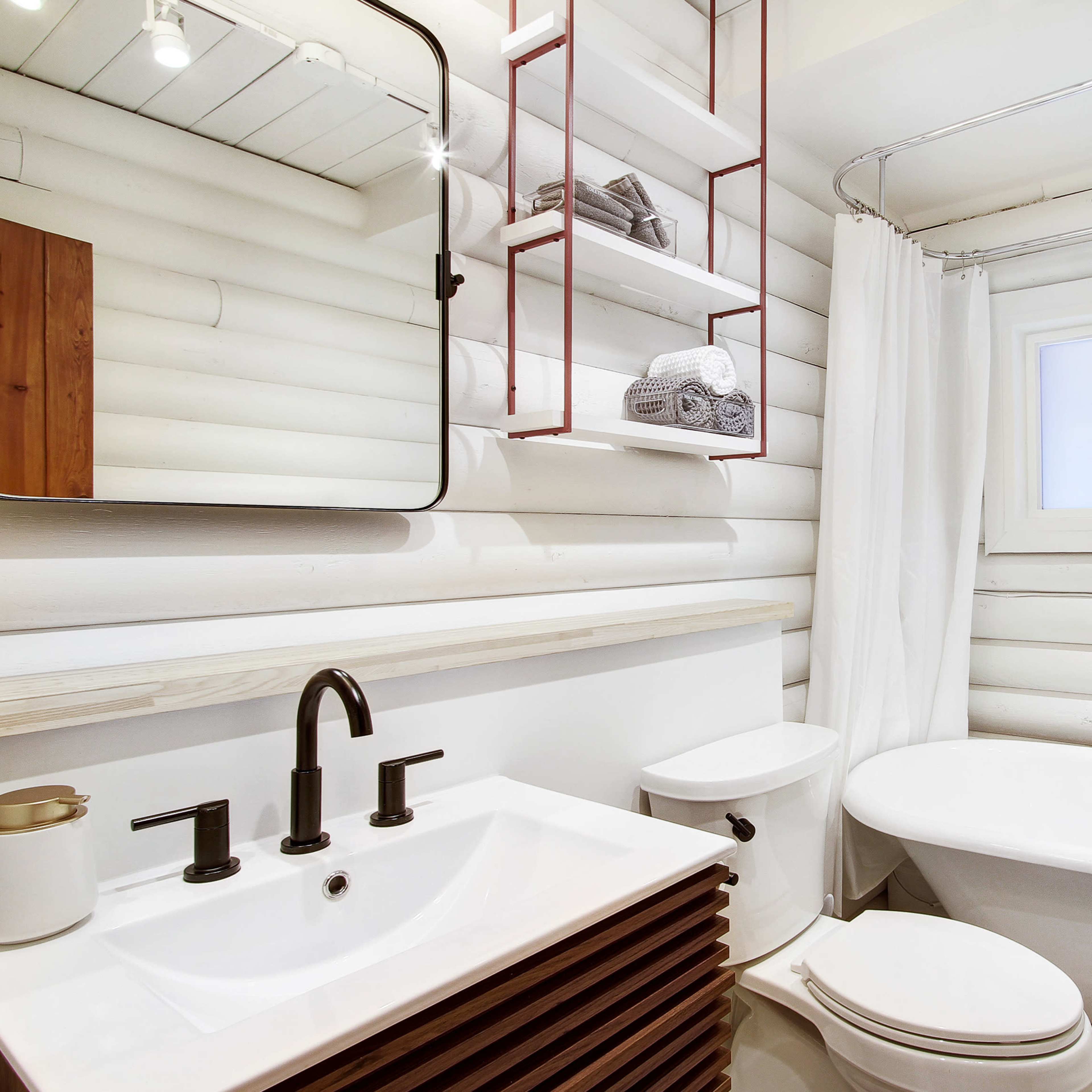 A modern bathroom featuring a freestanding bathtub, a wall-mounted mirror, and wooden shelving against white paneling.