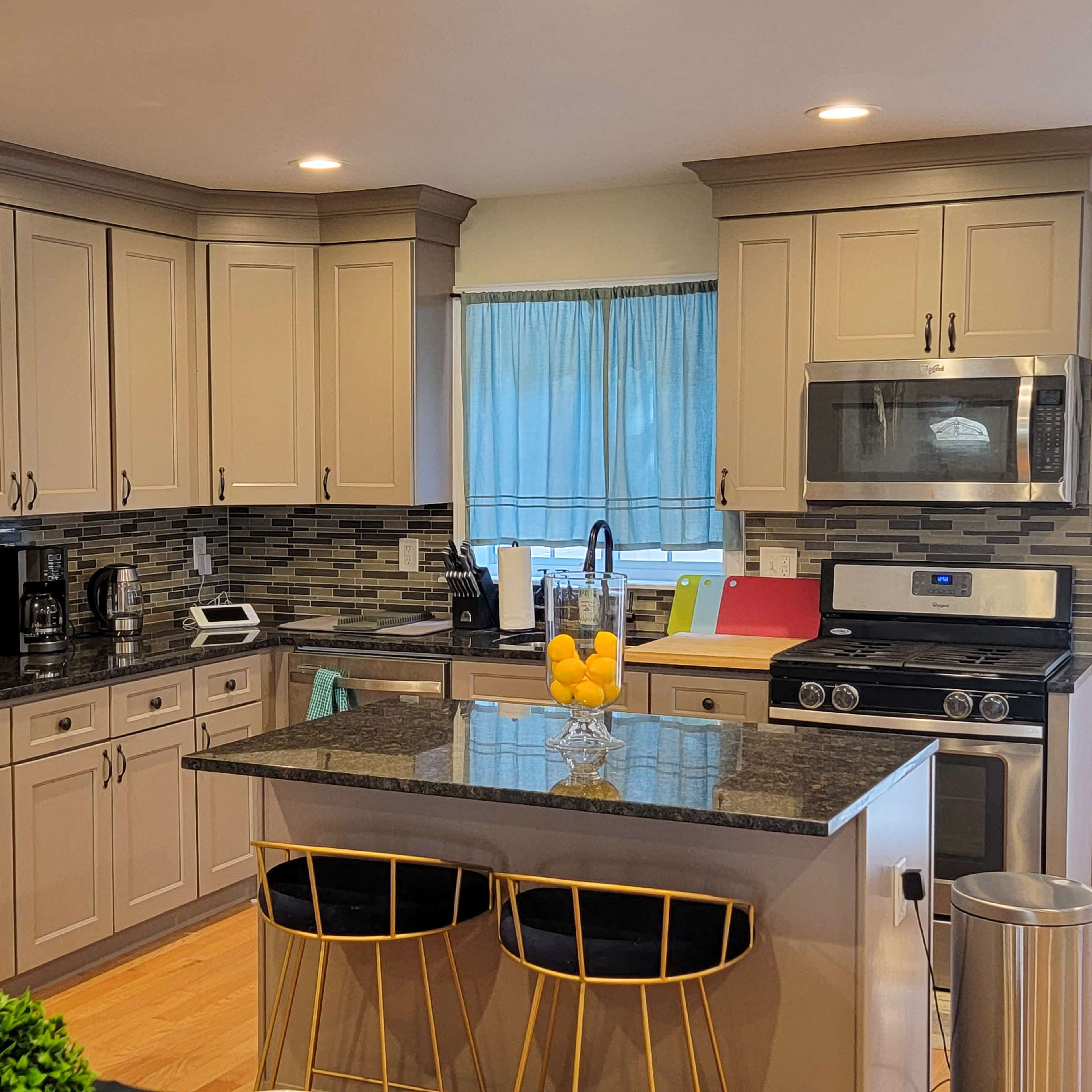 A modern kitchen with gray cabinets, stainless steel appliances, and a central island with yellow bar stools.