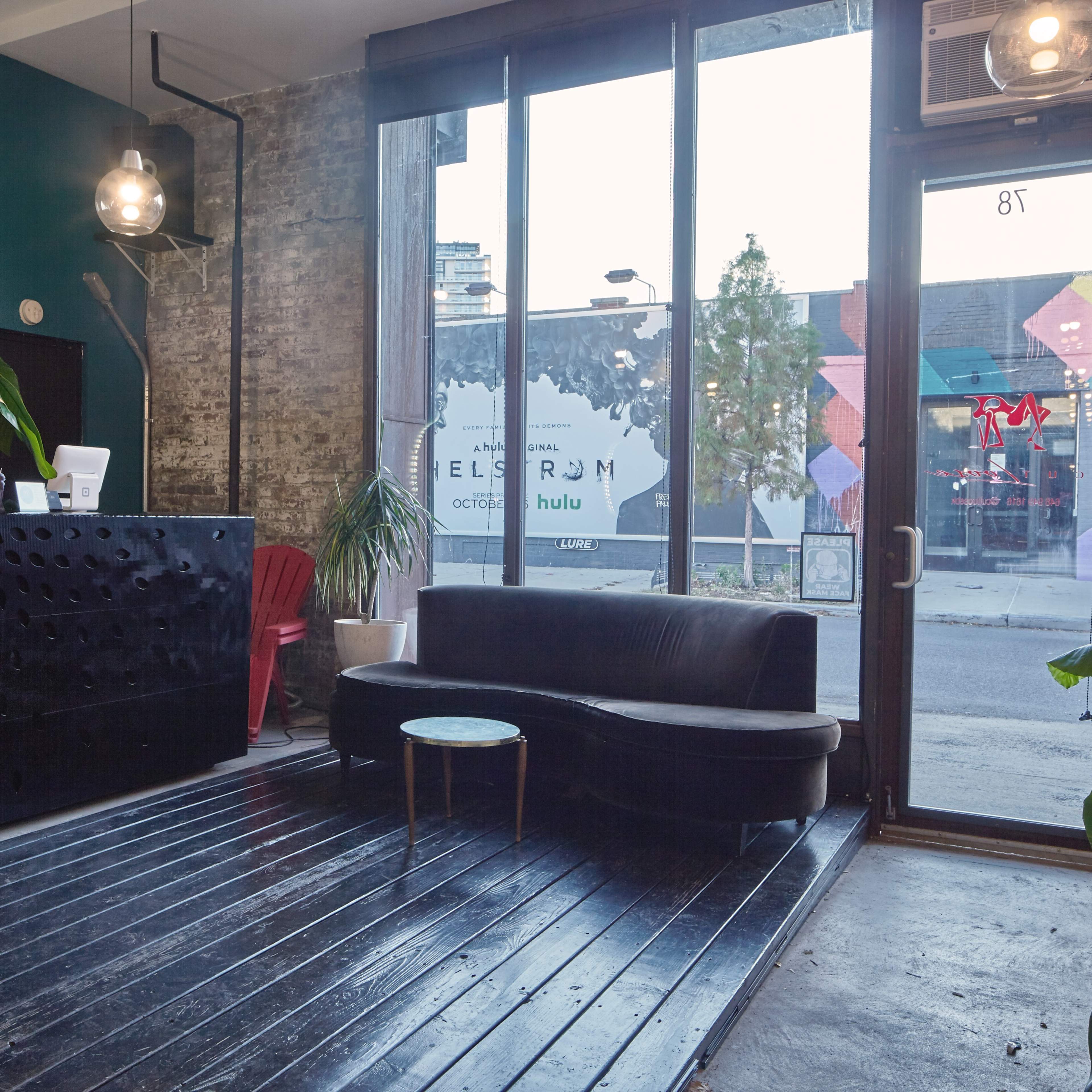 A modern reception area with a black couch, a coffee table, and large windows displaying a street view.