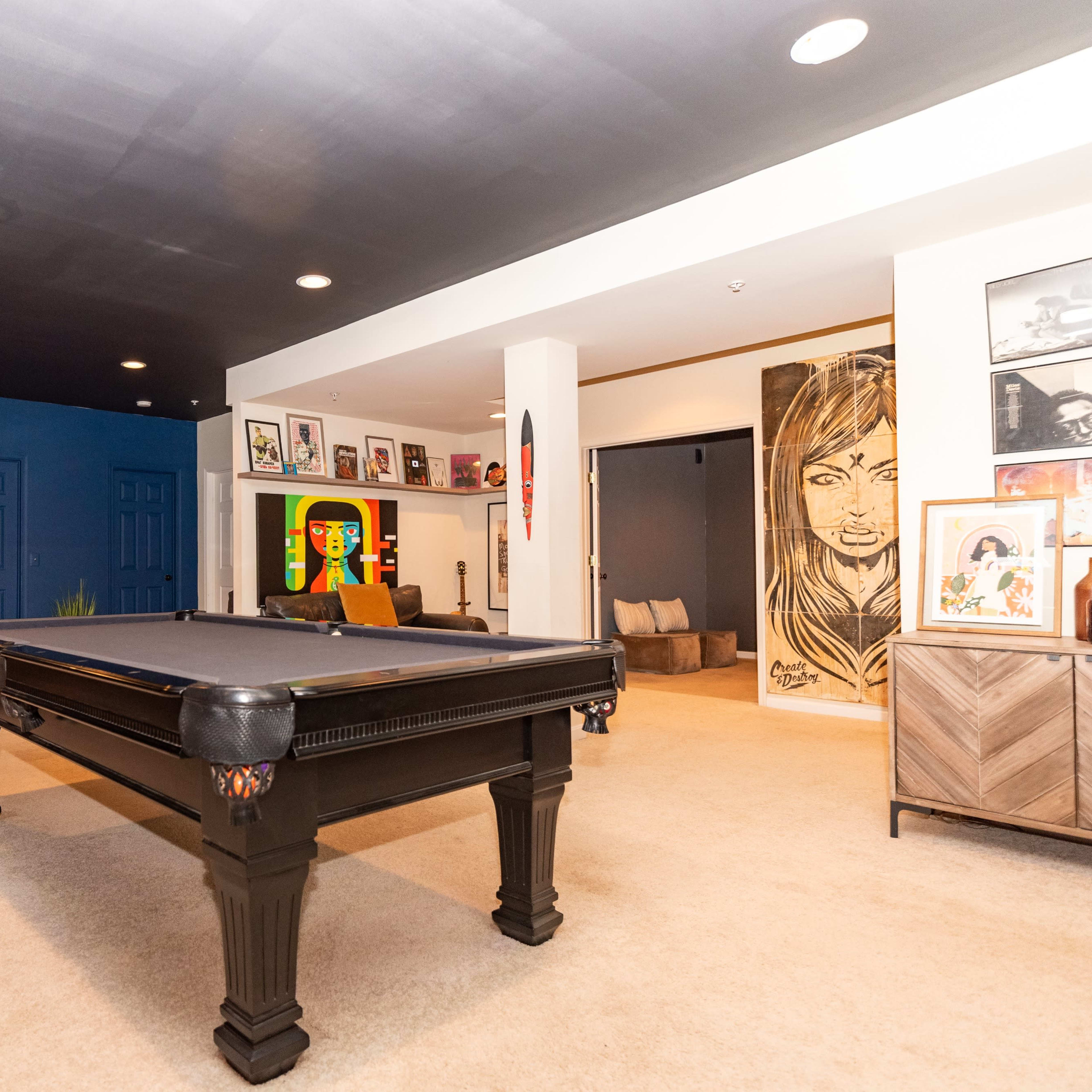 A spacious room featuring a black pool table at the center, surrounded by various artworks and seating areas.