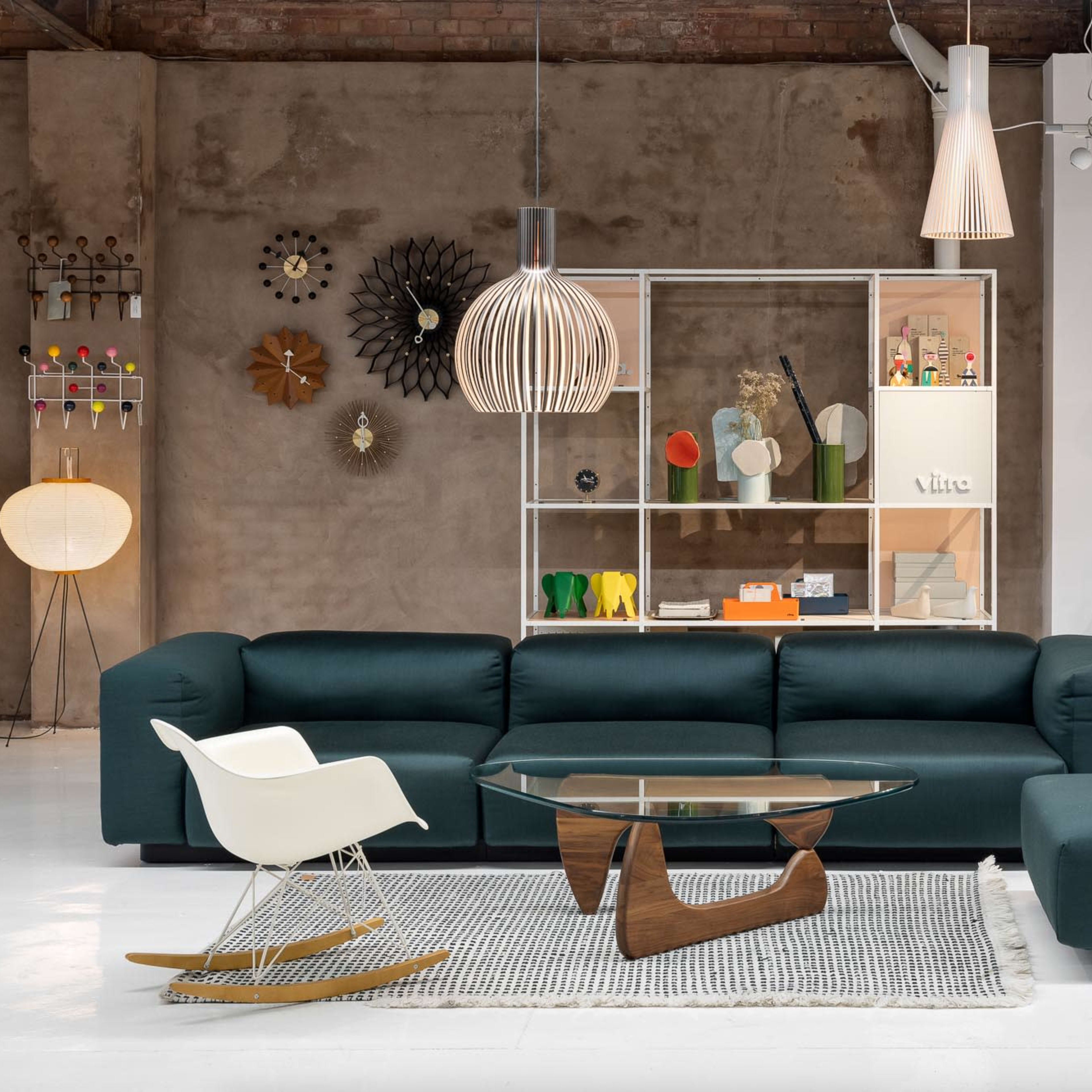 A modern living room with a dark green sofa, a glass coffee table, a contemporary rocking chair, and a variety of accent chairs displayed on the wall.