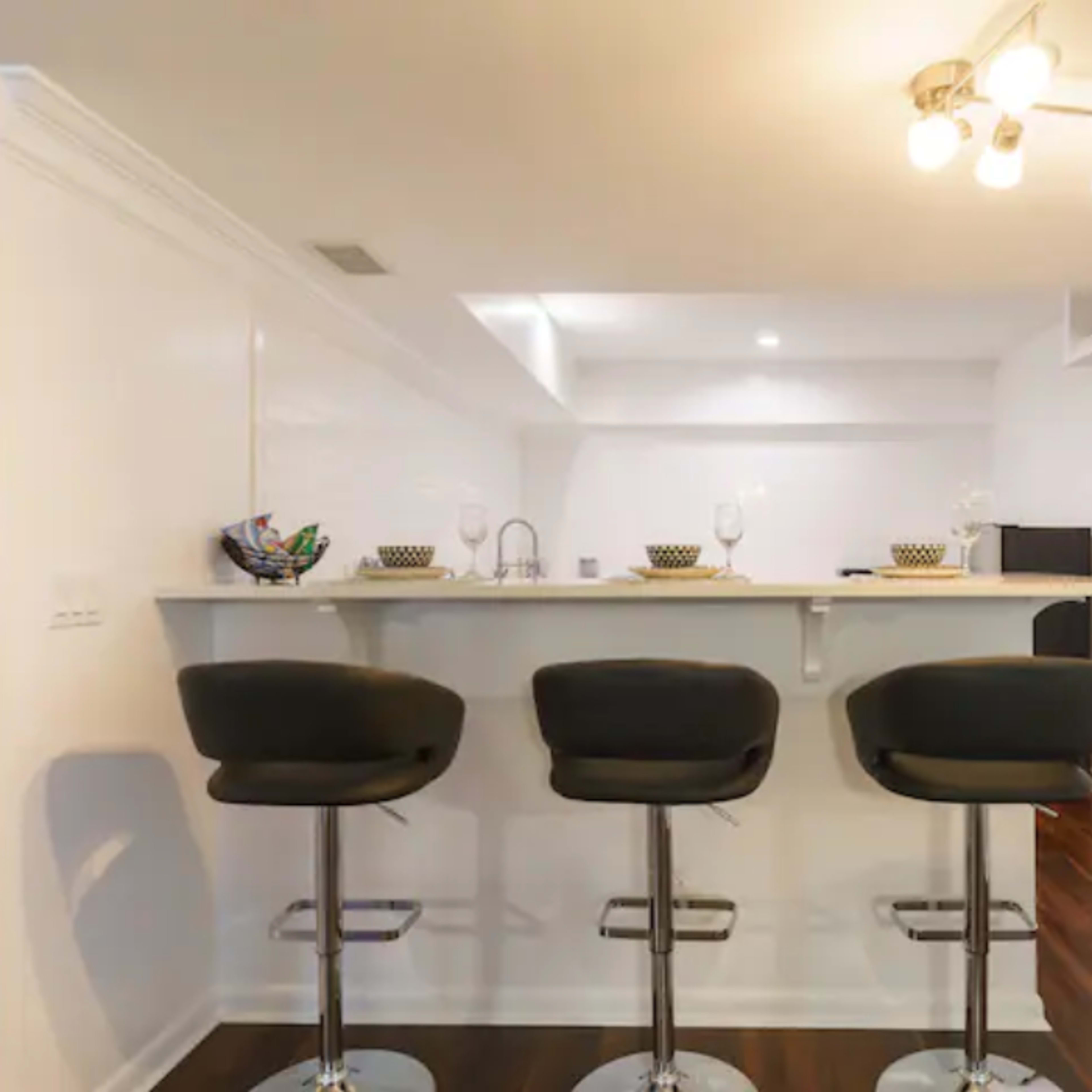 A modern kitchen bar features three black stools and a white countertop under a bright ceiling light.