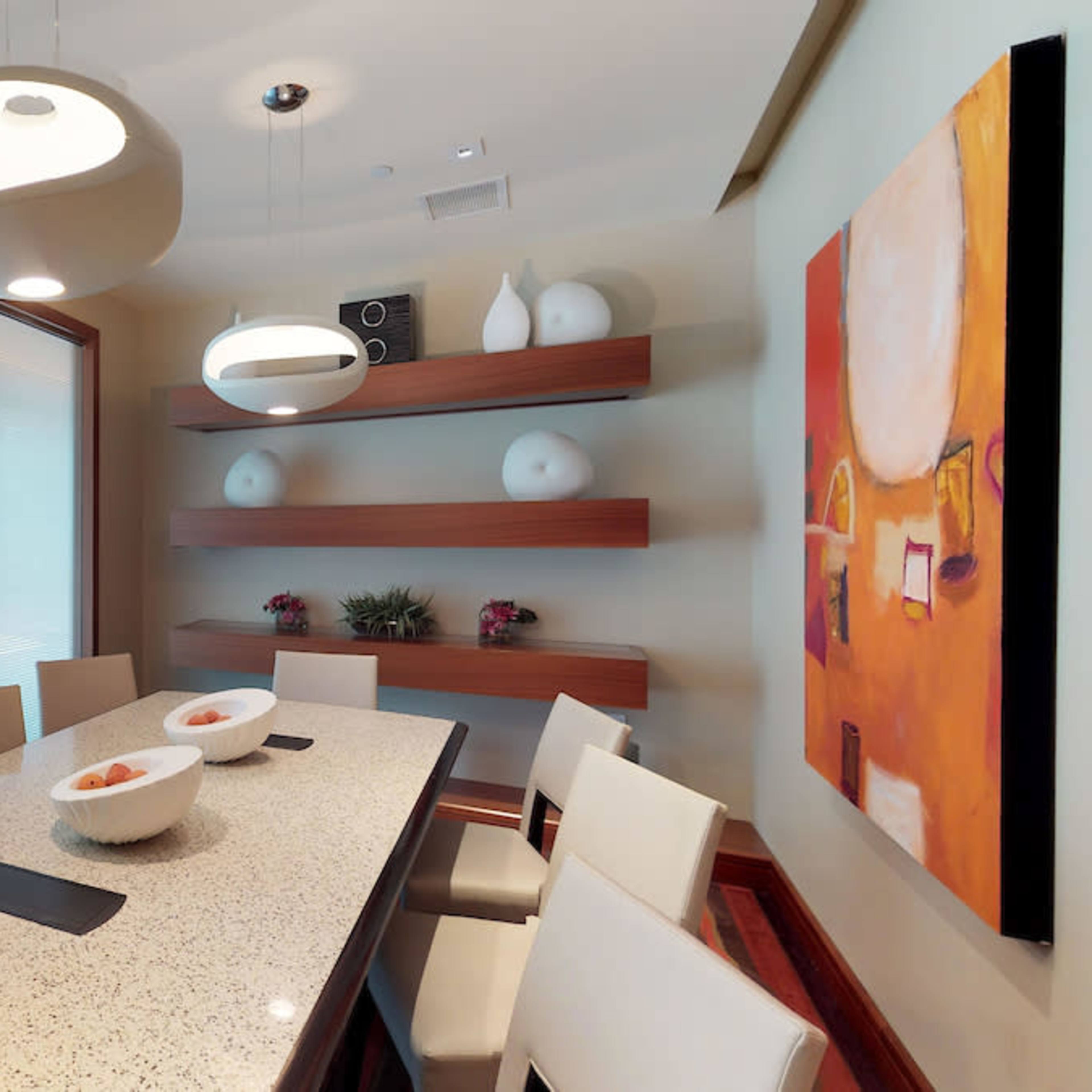 A modern dining area features a long table surrounded by chairs, with a large window and artistic decor on the walls.