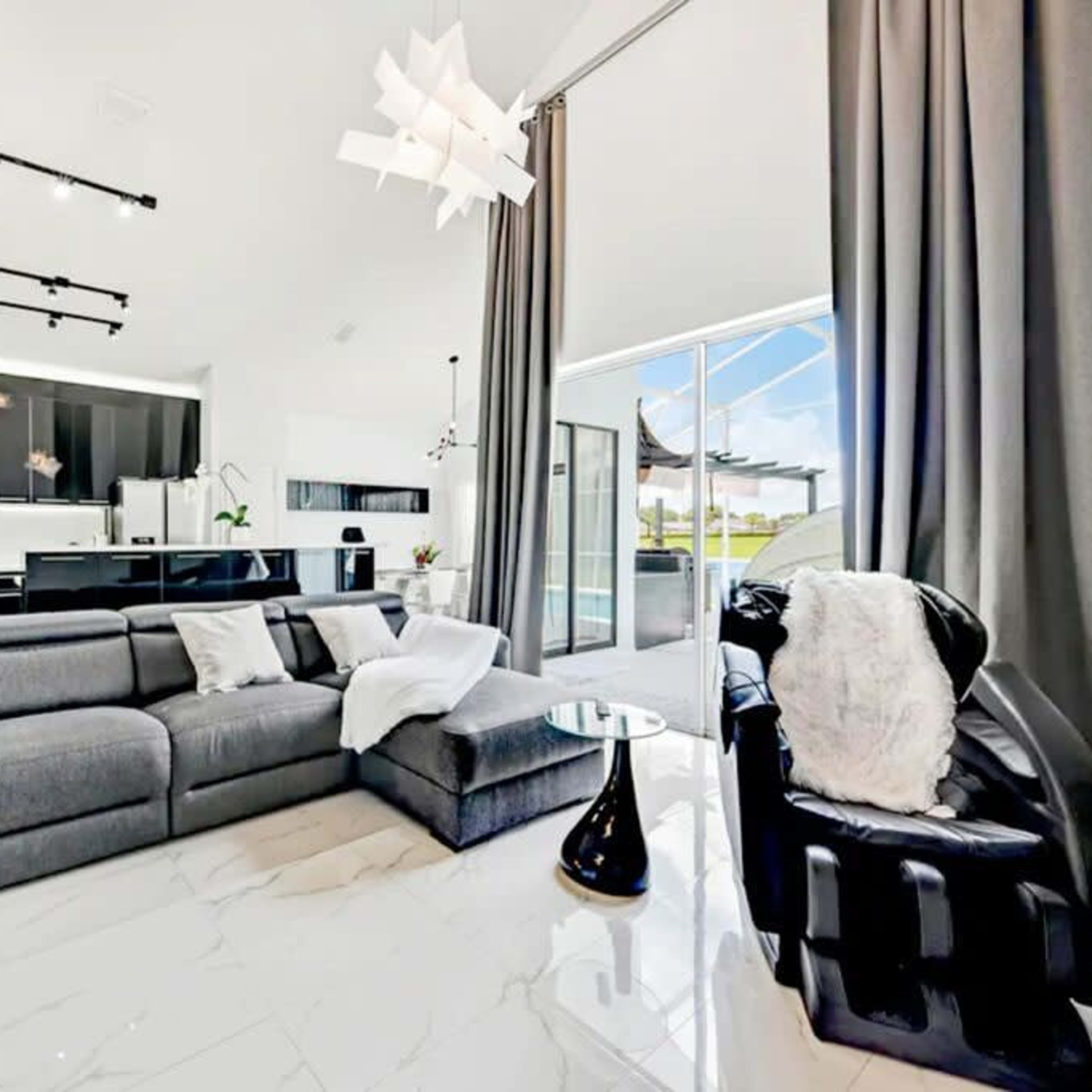 A modern living room featuring a gray sectional sofa, a black armchair, and large windows that provide natural light.