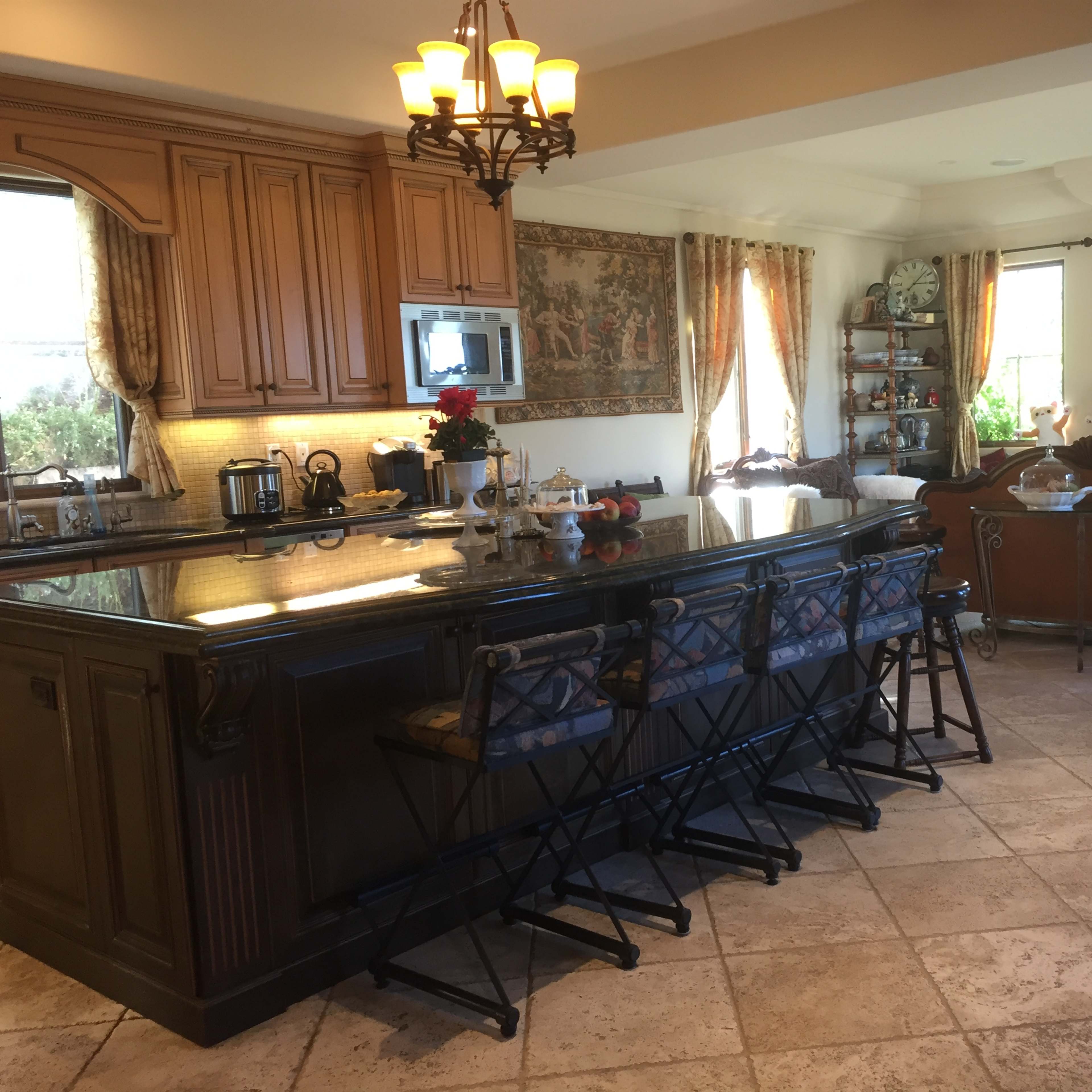 A spacious kitchen with wooden cabinets, a large island with bar stools, and an open layout leading into a living area with a television.