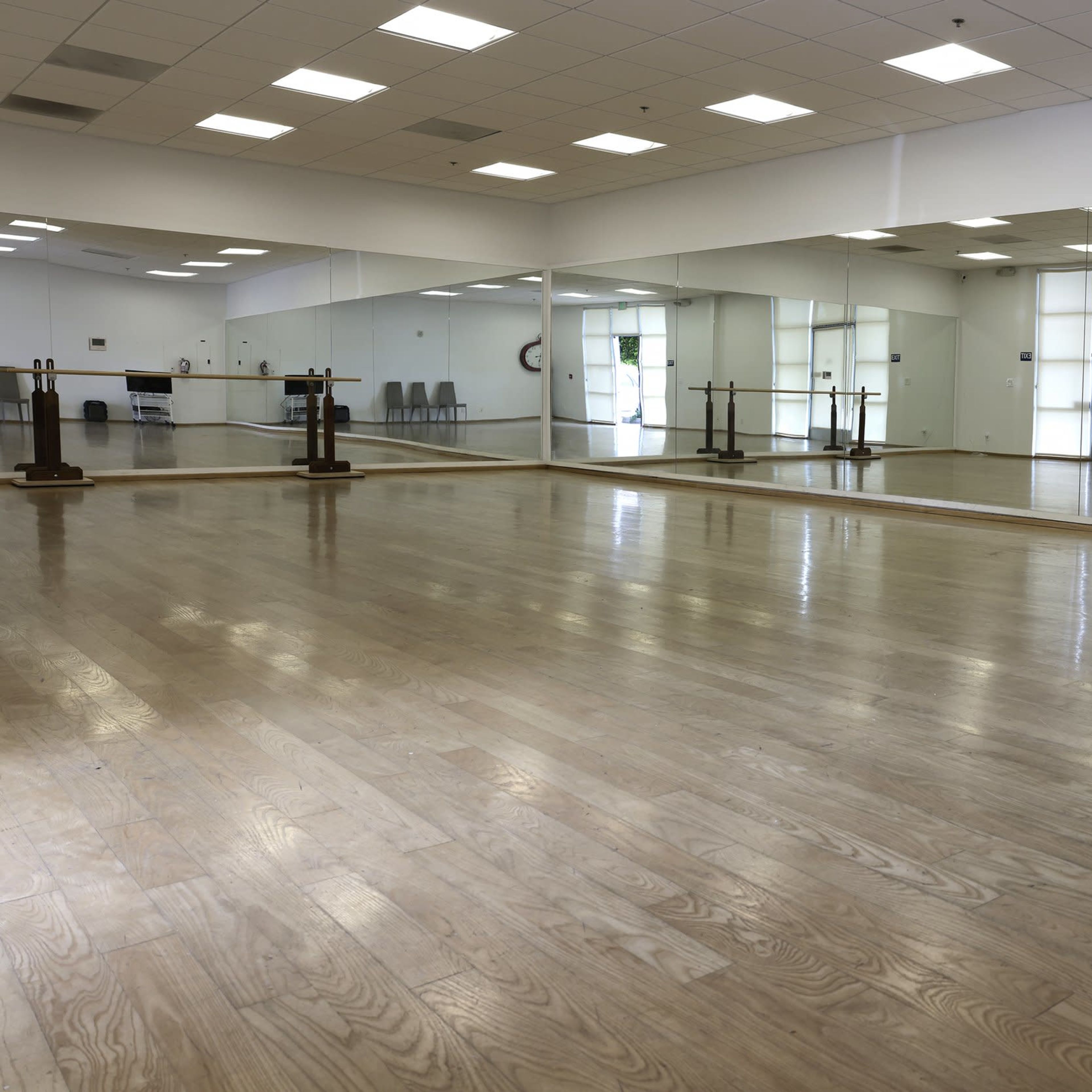 A spacious dance studio with wooden floors, large mirrors on one wall, and doors leading to an outside area.