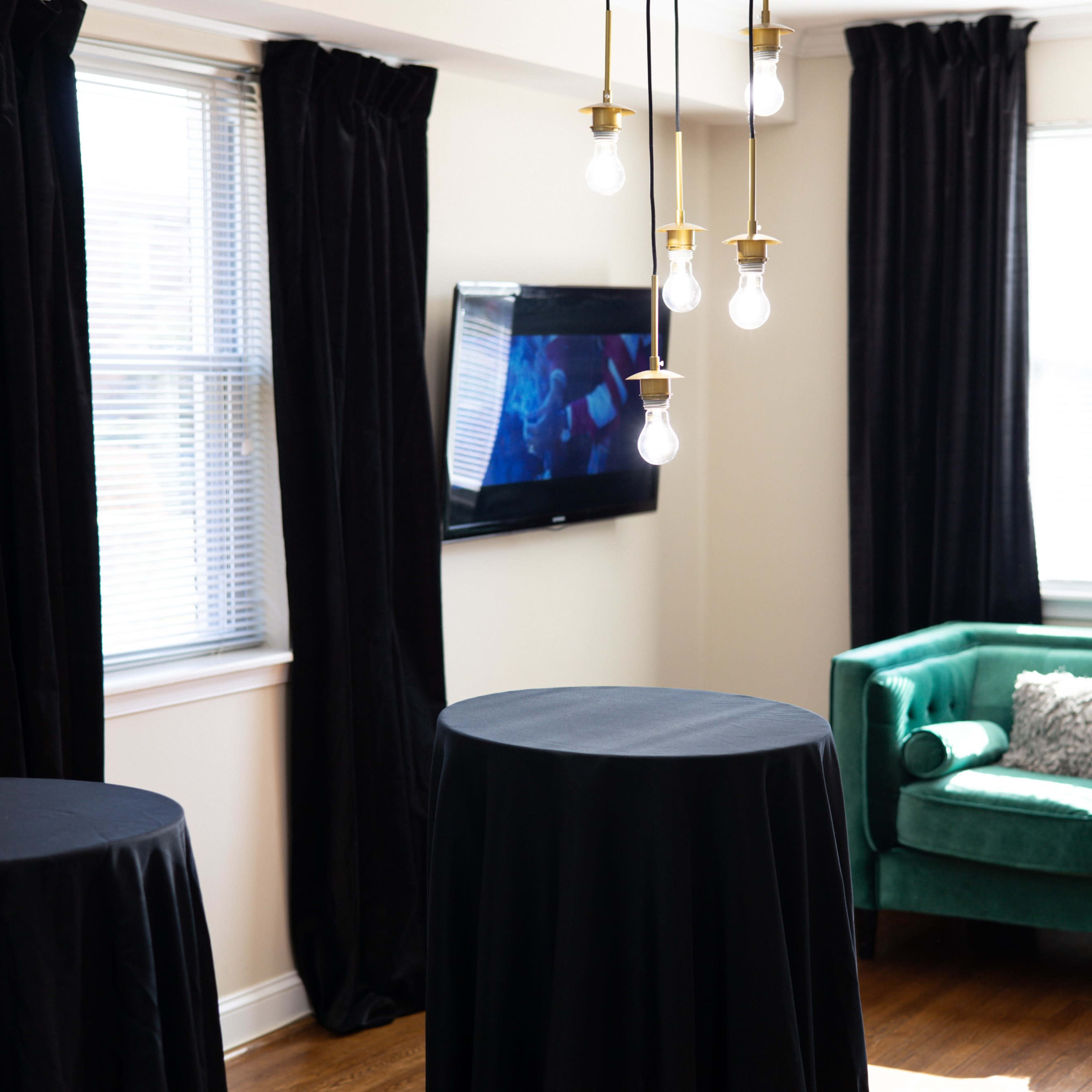 A well-lit room featuring two tall black tables, a green sofa, and a television mounted on the wall.
