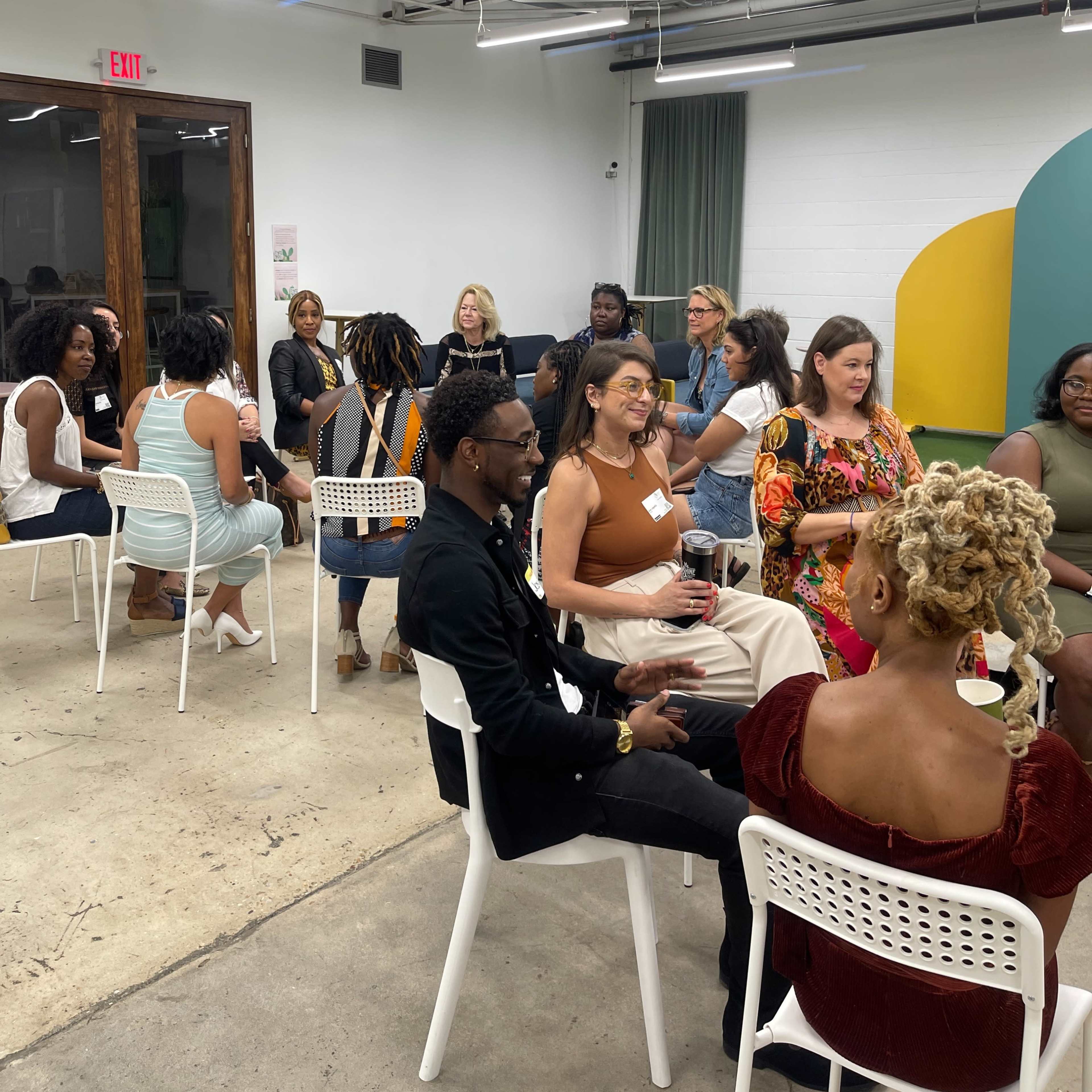 A group of diverse individuals is engaged in conversation while seated in a modern, brightly lit room.