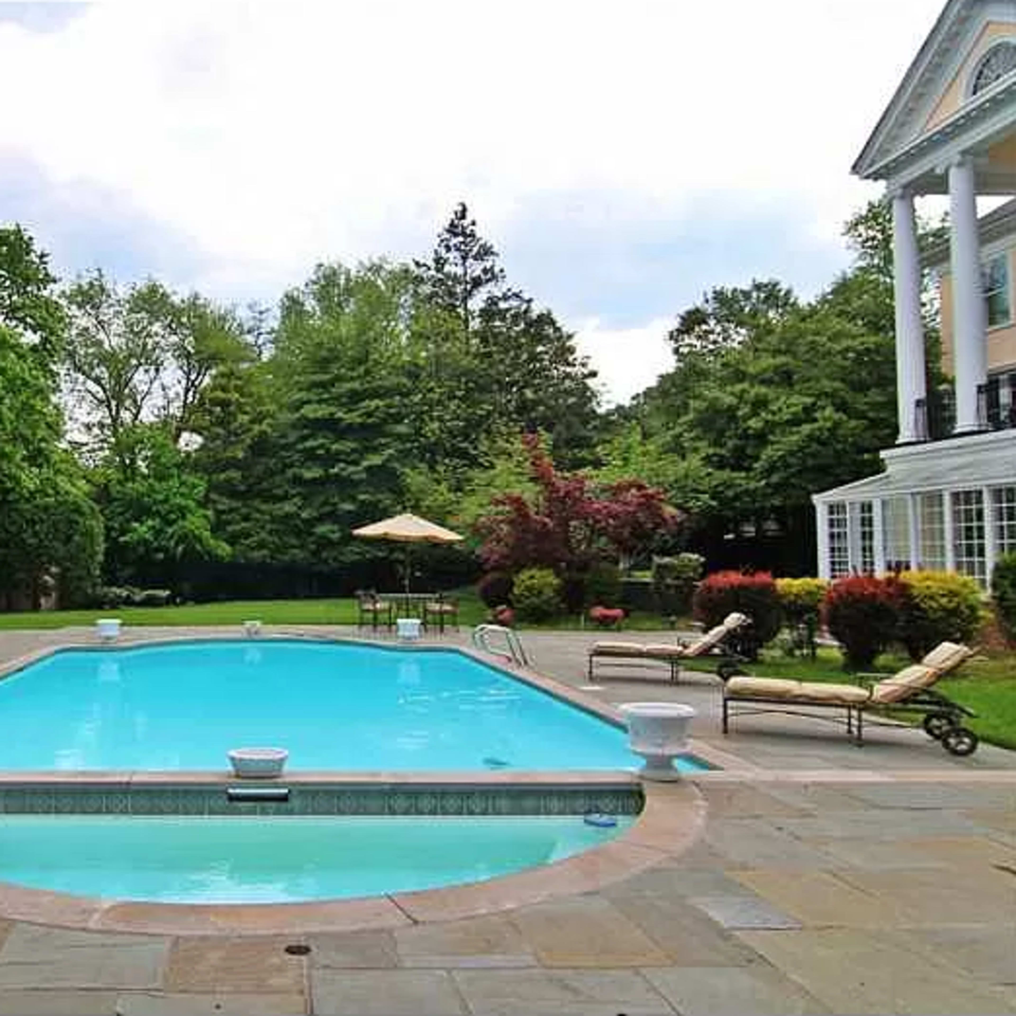 A rectangular swimming pool surrounded by lounge chairs and lush greenery in a landscaped backyard.