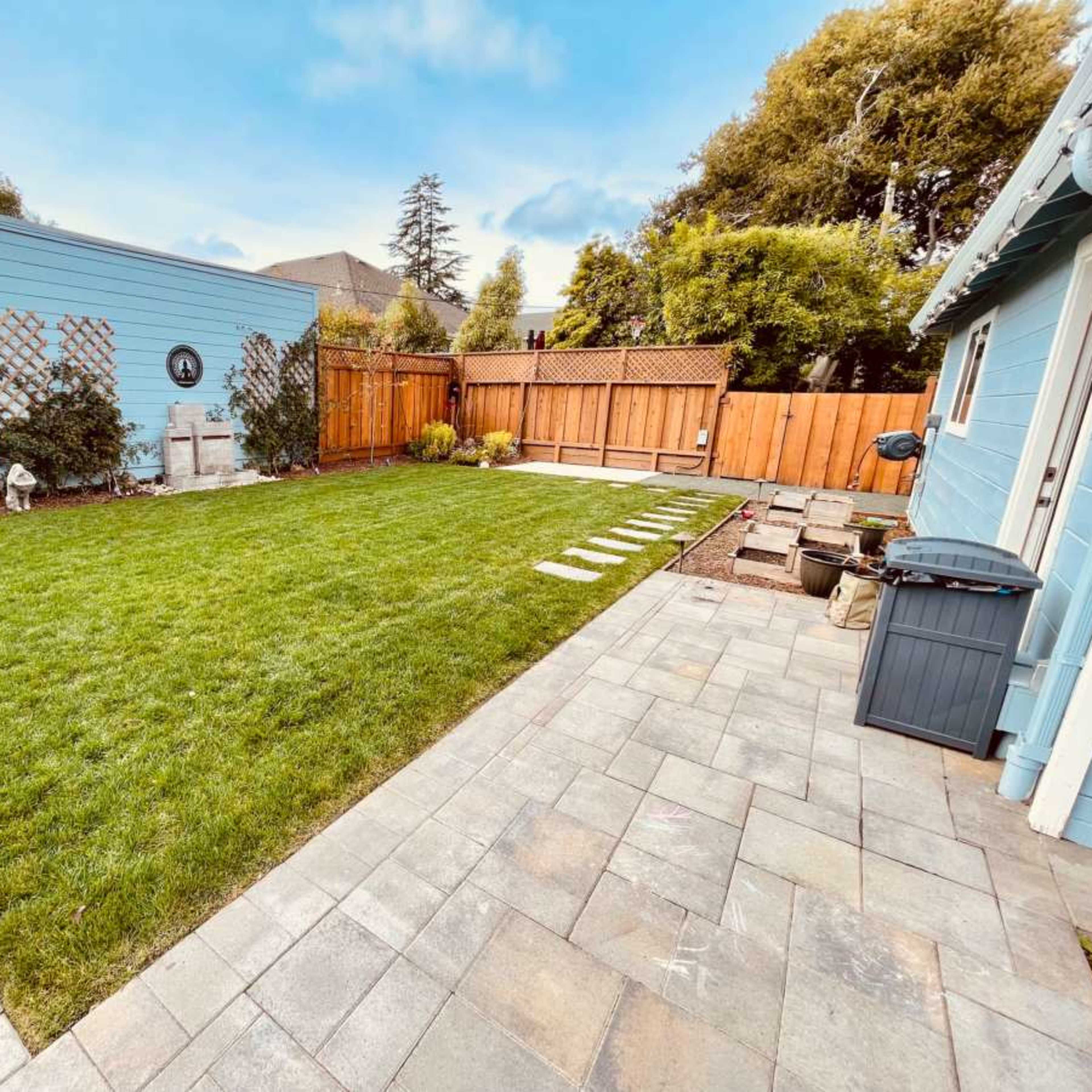 A well-maintained backyard with a grassy area bordered by stone paving and wooden fences.
